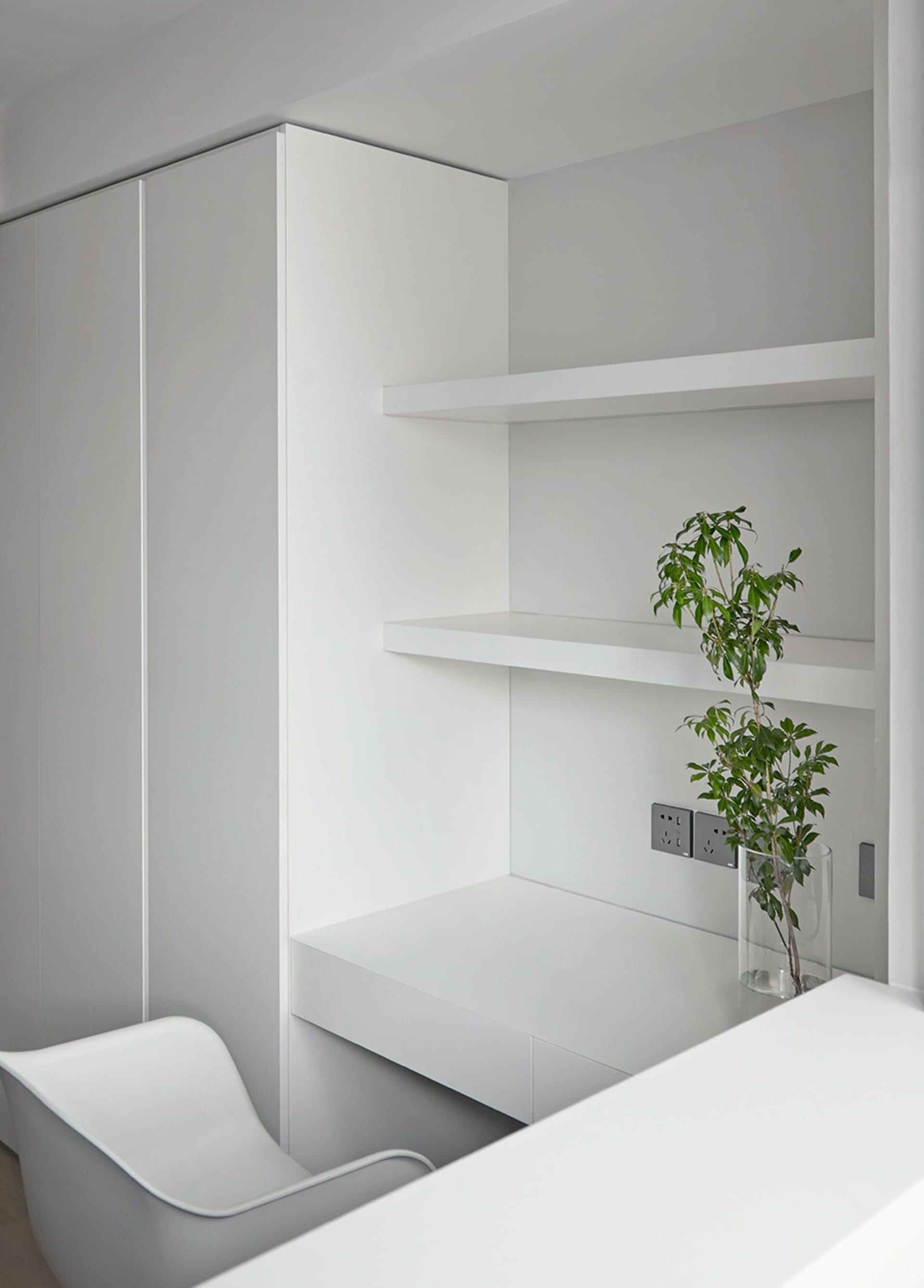 Minimalist office space with white shelves and desk, grey chair, and green plant.