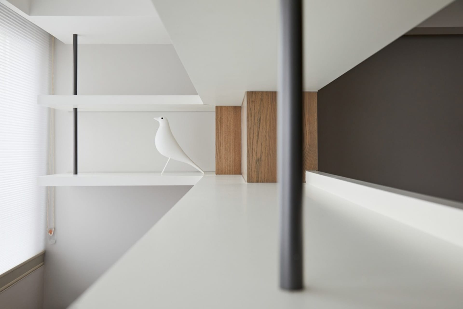 A modern wooden shelf with a white bird figurine on it, located next to a window with blinds.