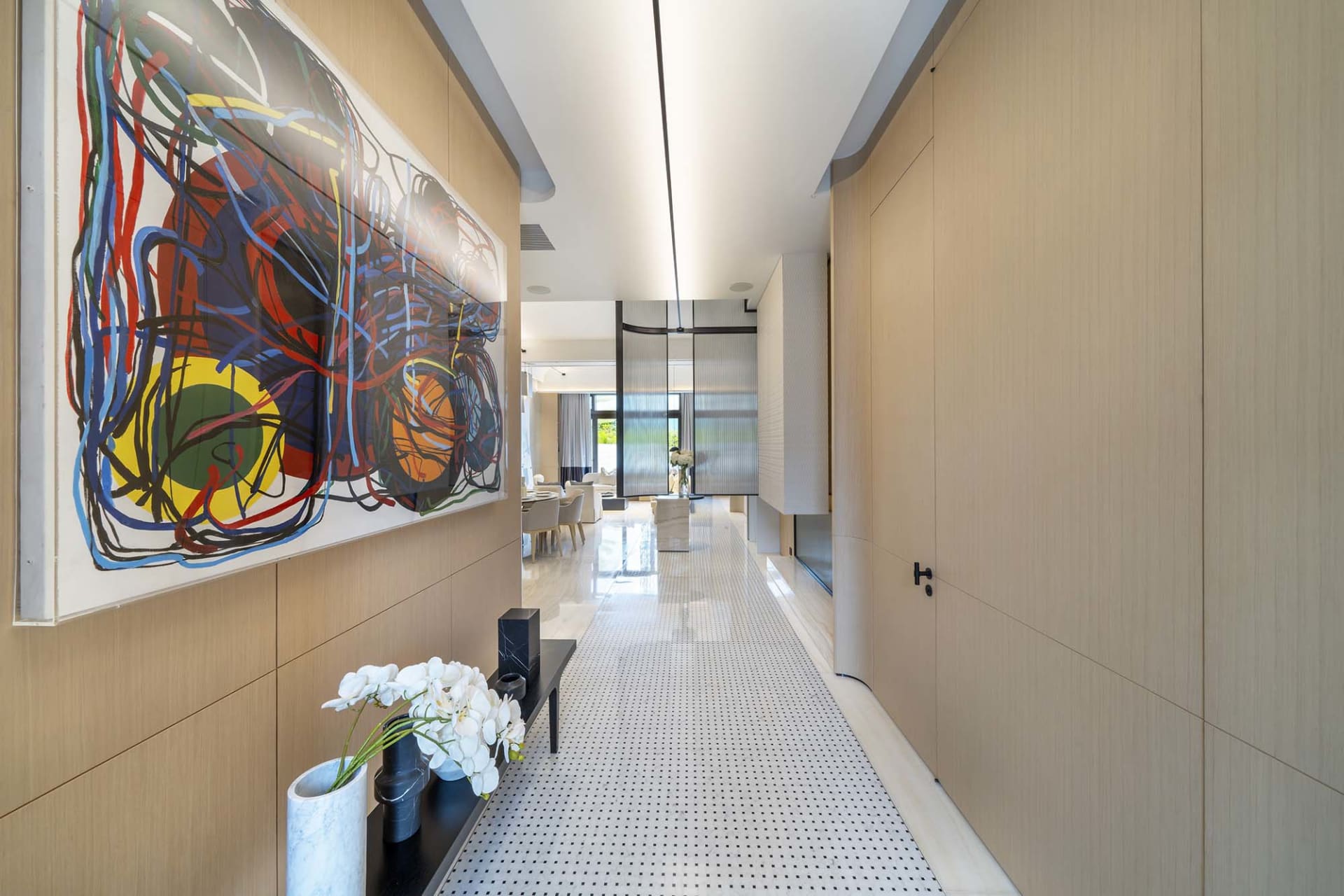 A minimalist modern interior hallway with a large abstract painting on the left and a minimalist bench with orchids and vases