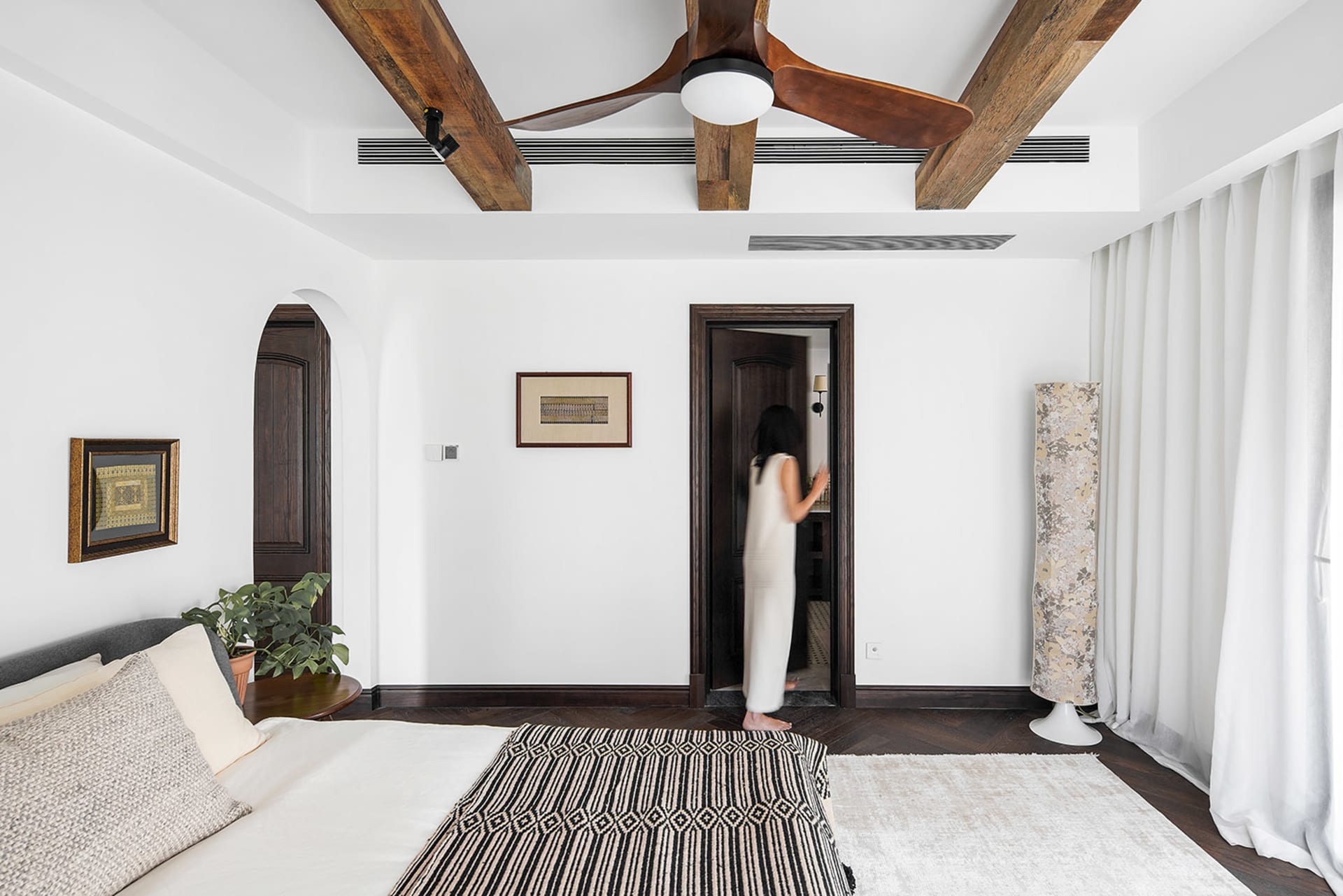 A modern bedroom with a wooden ceiling fan, white walls, and a white rug with black patterns.