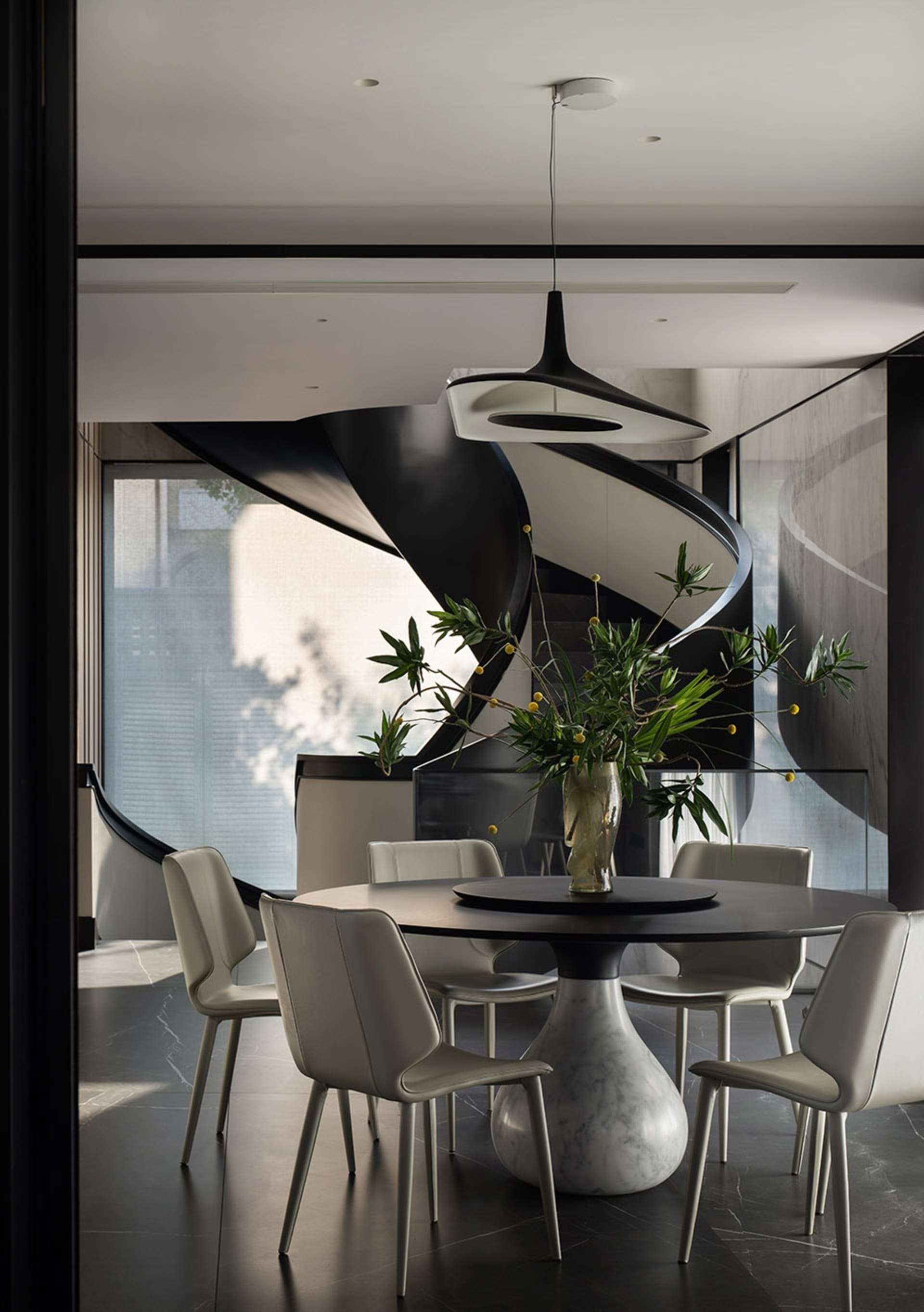 Modern dining room with marble table and chairs, featuring a contemporary light fixture and a vase of greenery.