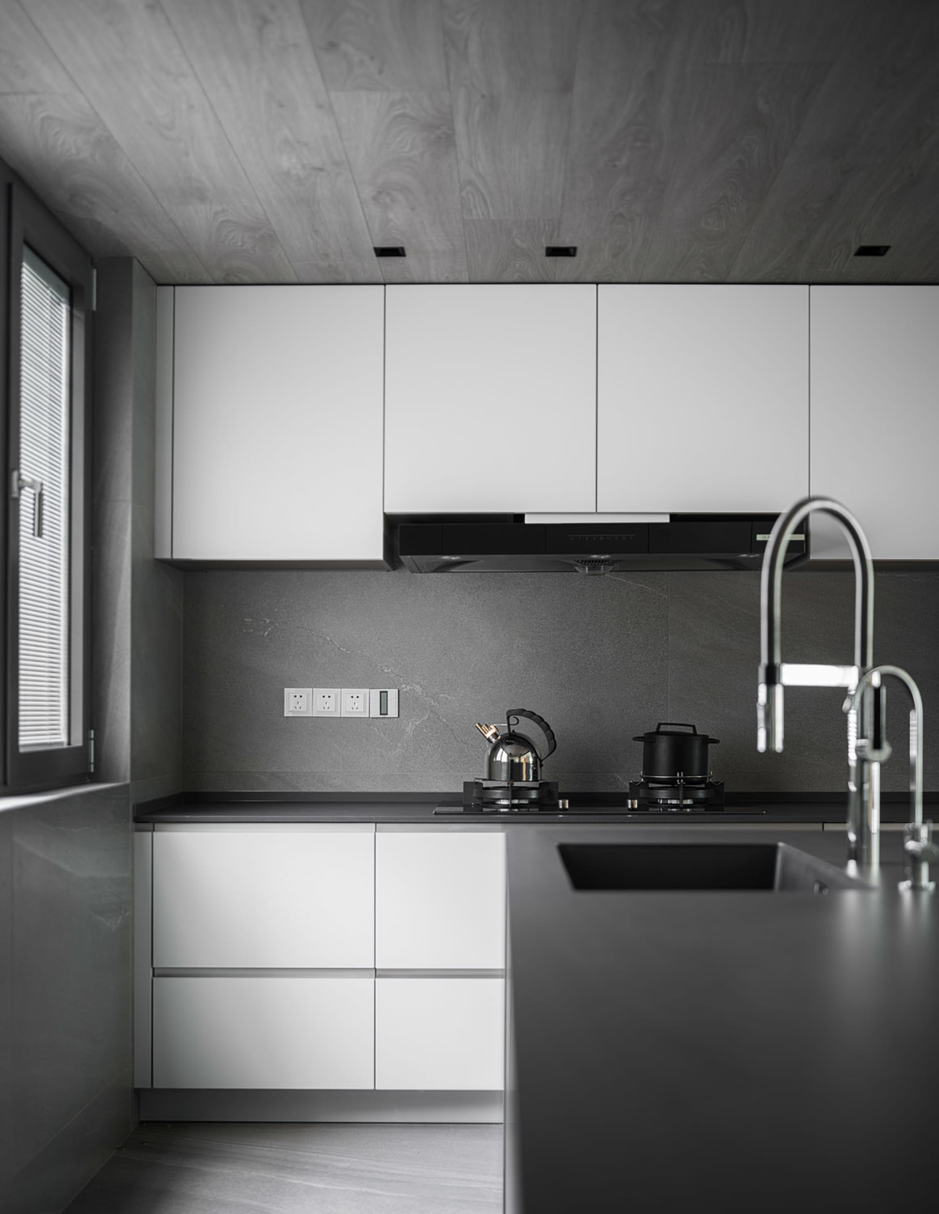A modern kitchen featuring concrete walls and marble countertops with white cabinets and appliances.