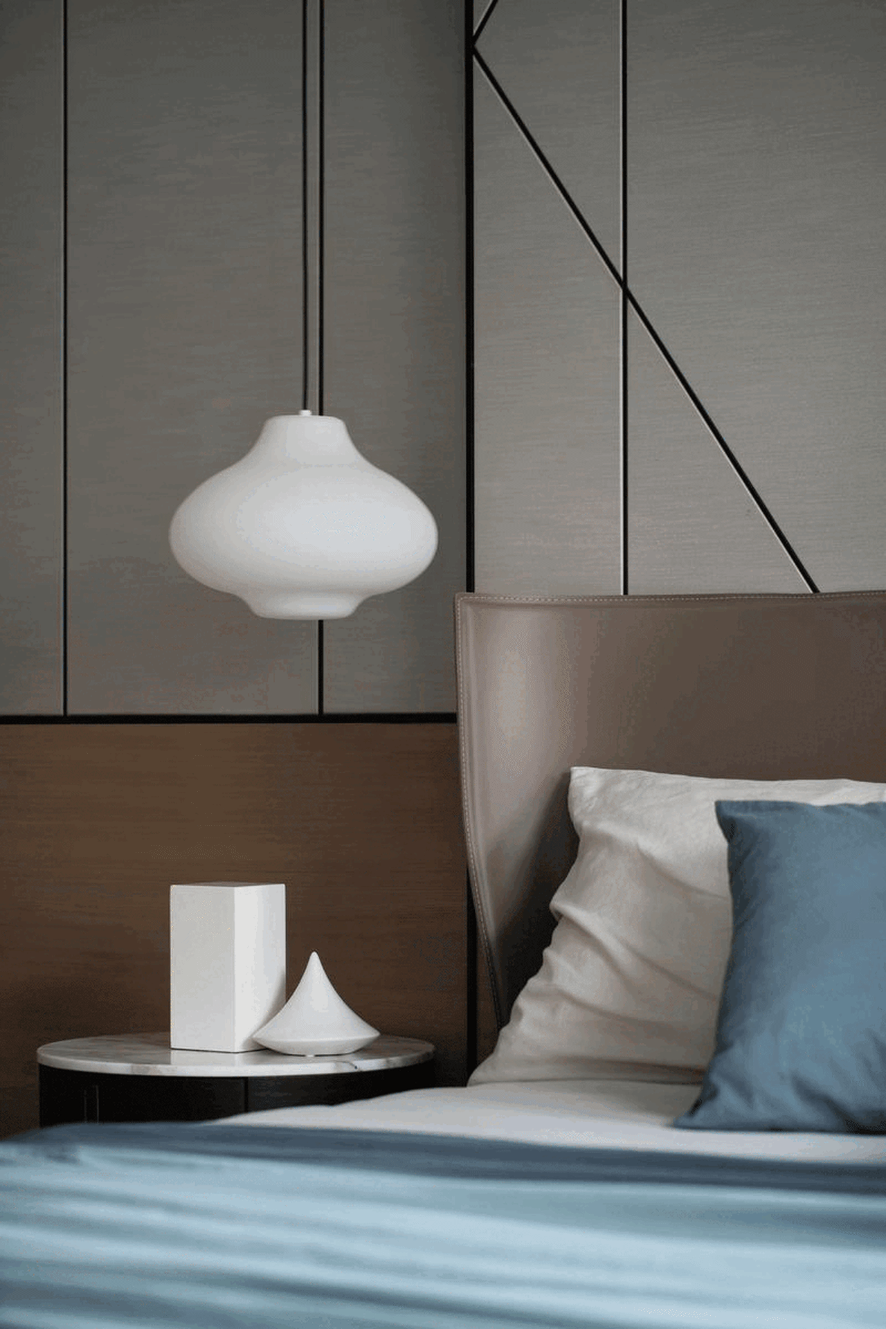 Modern minimalist bedroom featuring a leather headboard, glass pendant light, and wooden walls.