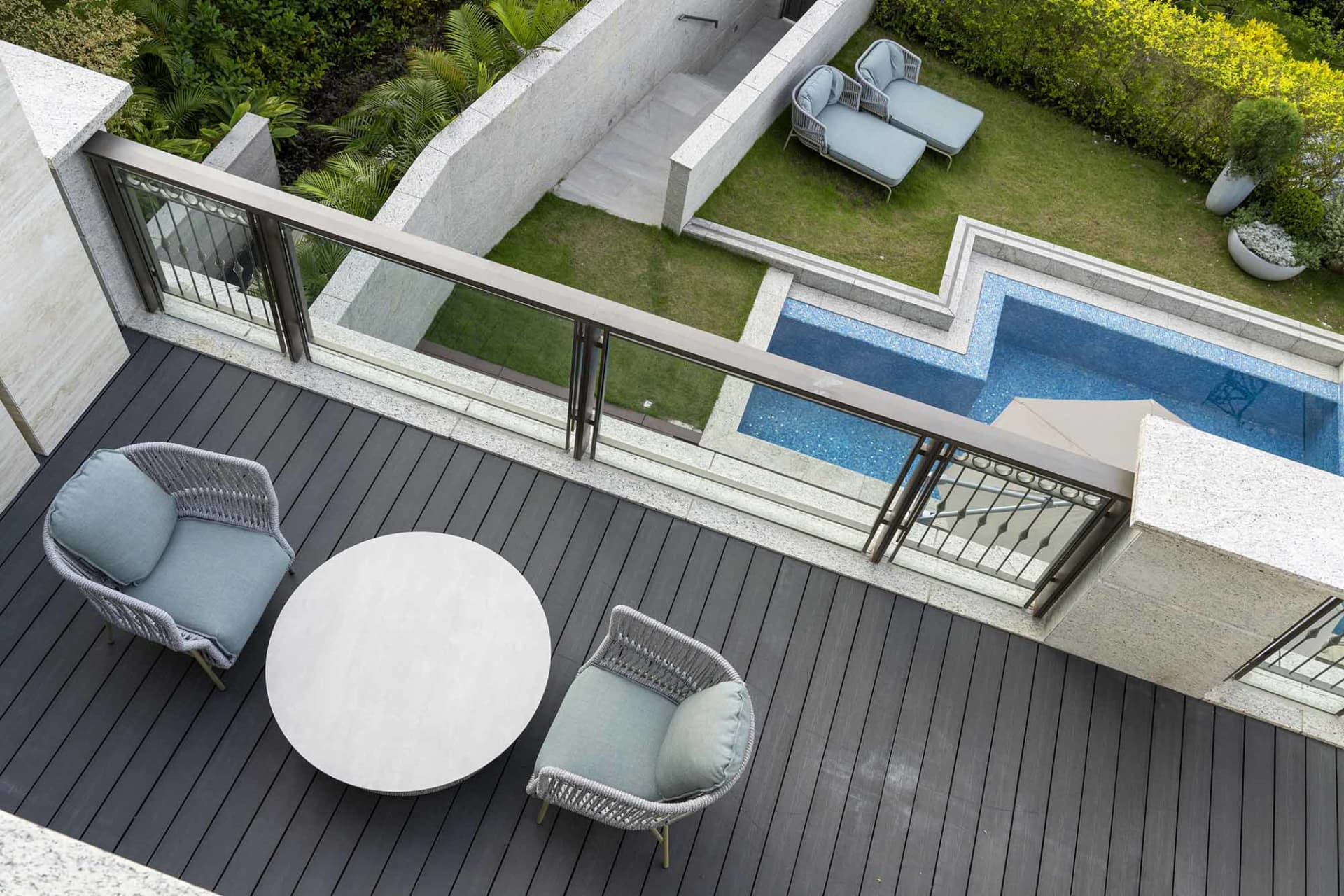 Modern patio with a round table and two chairs, featuring a concrete deck, glass railings, and a concrete wall with a glass w