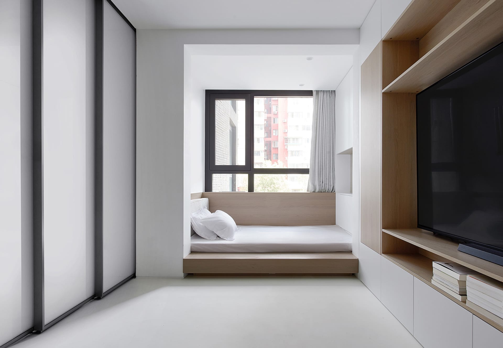 A minimalist bedroom with a bed platform, window, and built-in shelves.