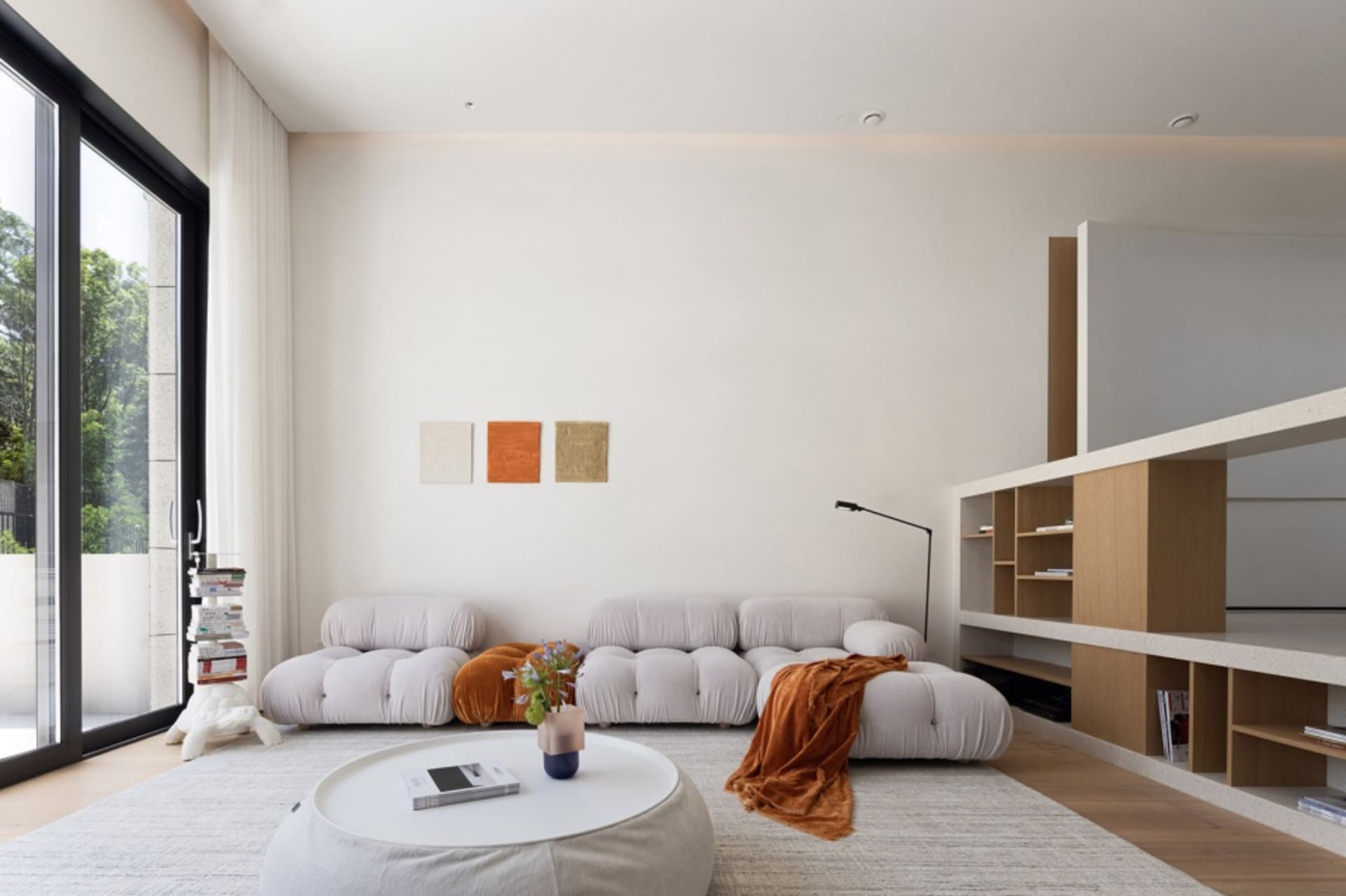 A minimalist living room with a white sofa, wooden shelves, and a white coffee table with a potted plant.