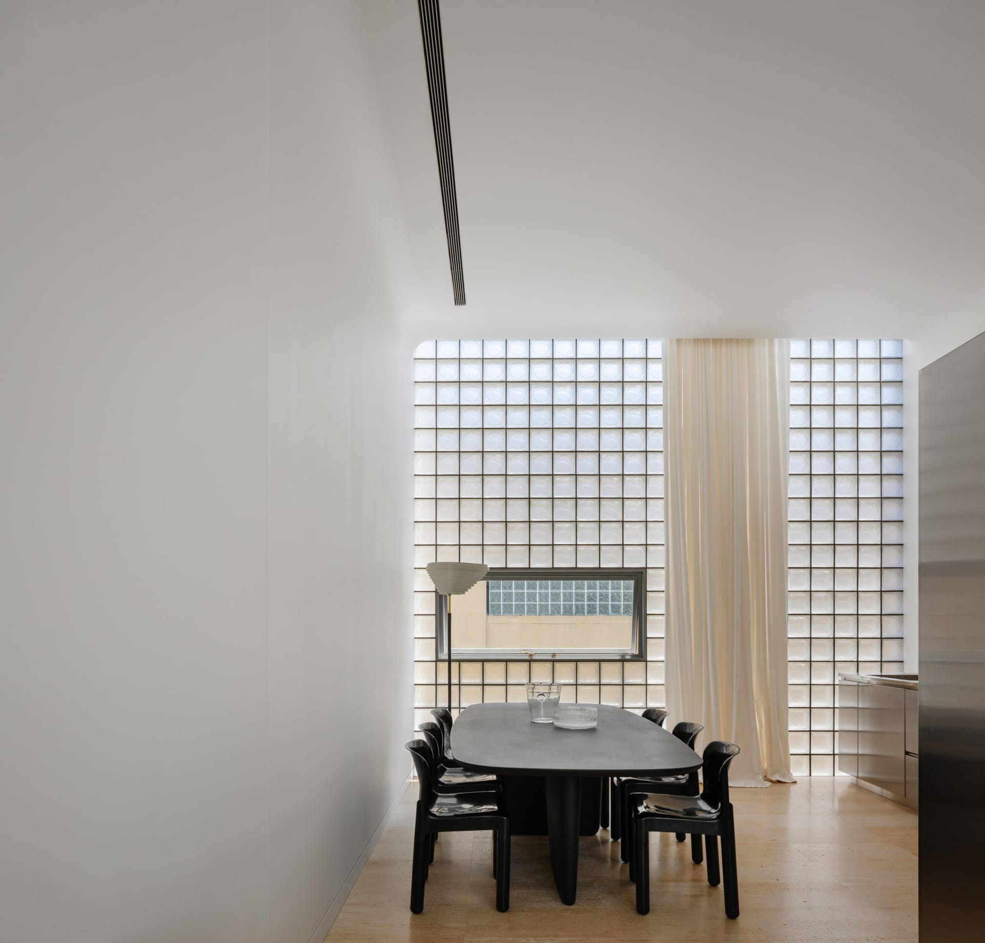 Modern dining room featuring glass block wall, wooden floor, and minimalist design.