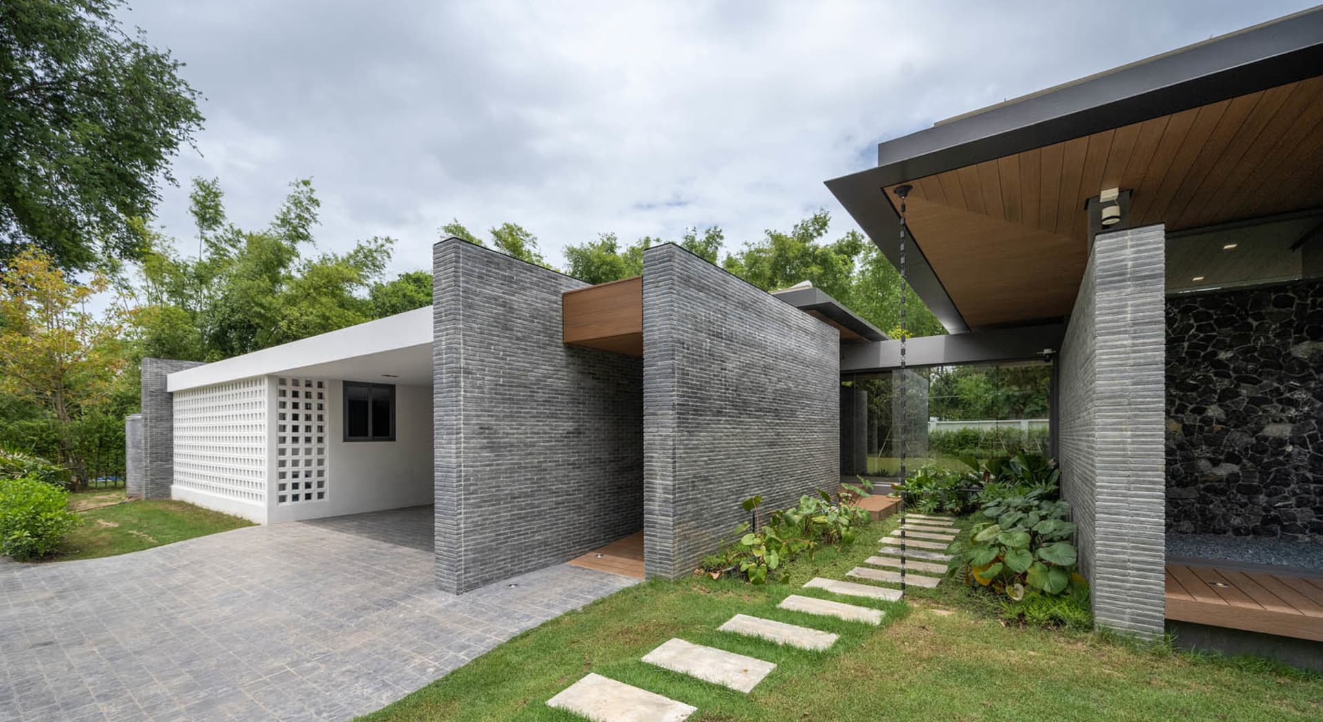Modern residential exterior featuring brick, tile, concrete, and wood materials.