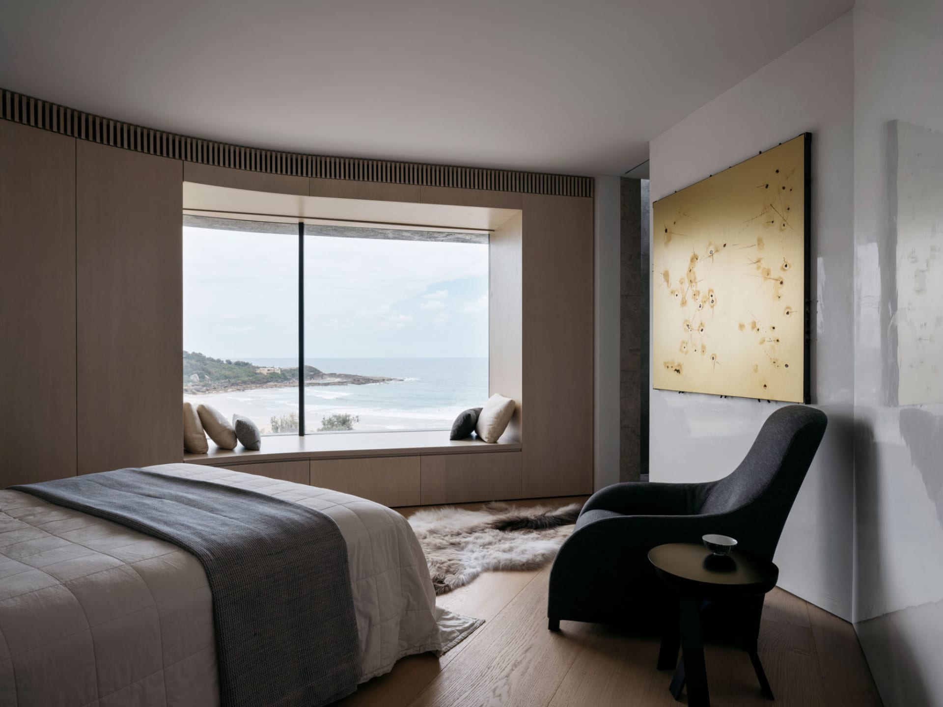 A contemporary bedroom with a large window overlooking the ocean, featuring a minimalist design with natural wooden elements.