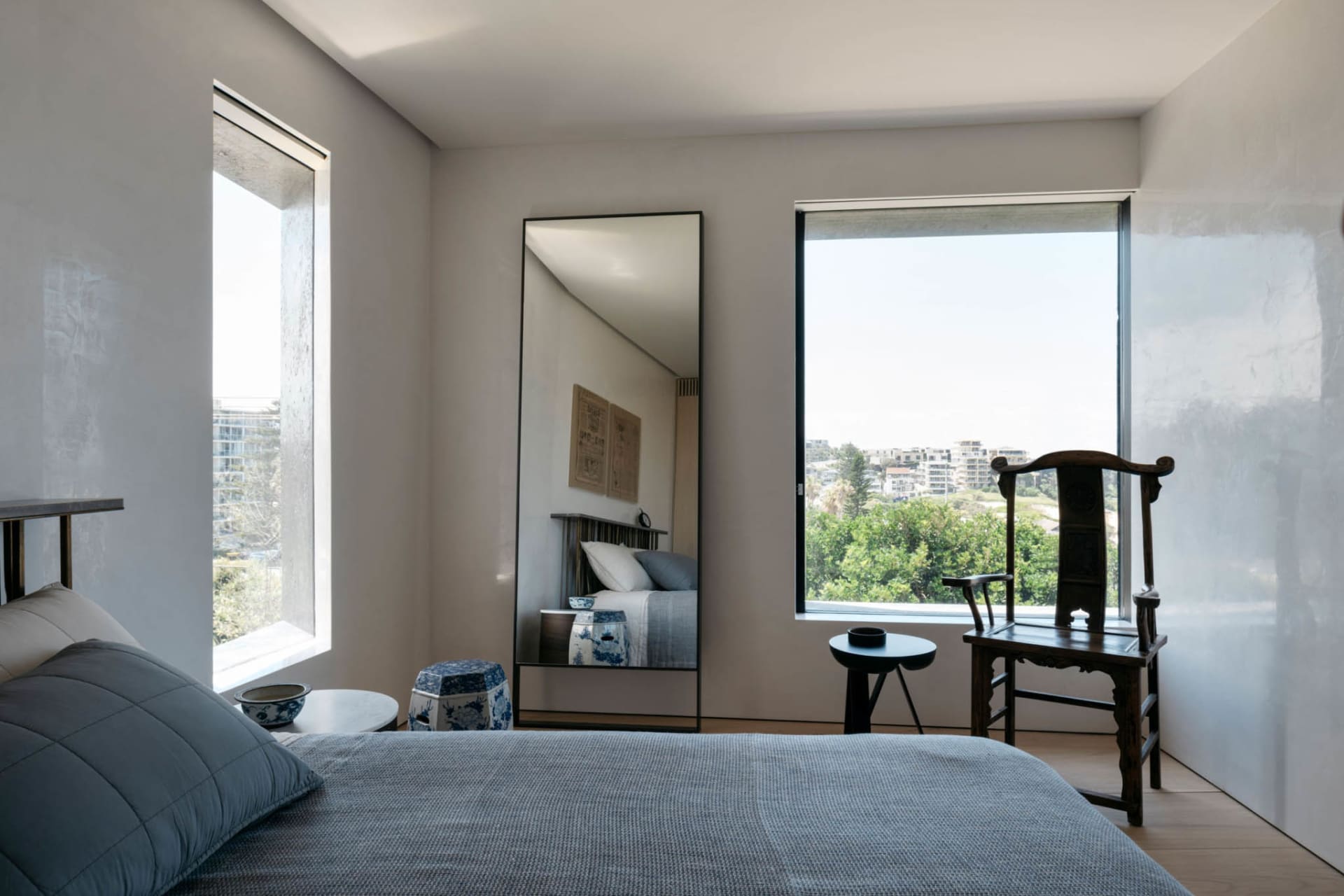 A minimalist bedroom featuring a blue bed and a large mirror.