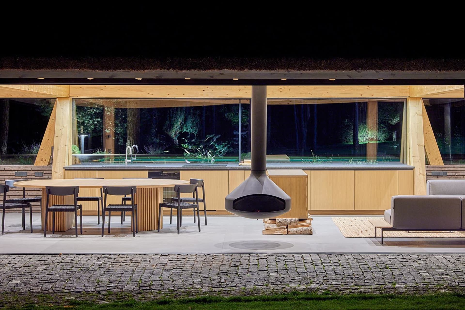 A modern outdoor kitchen with wooden elements and a hanging fireplace.
