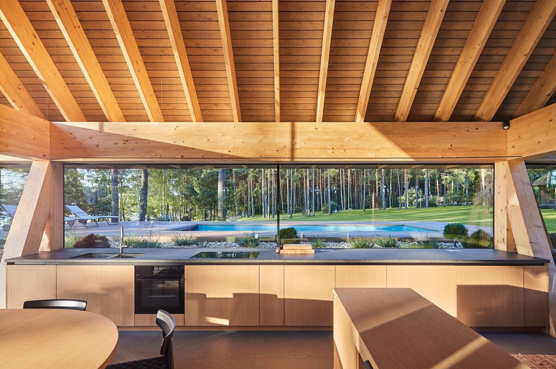 Modern outdoor kitchen with wooden elements and a swimming pool in the background.