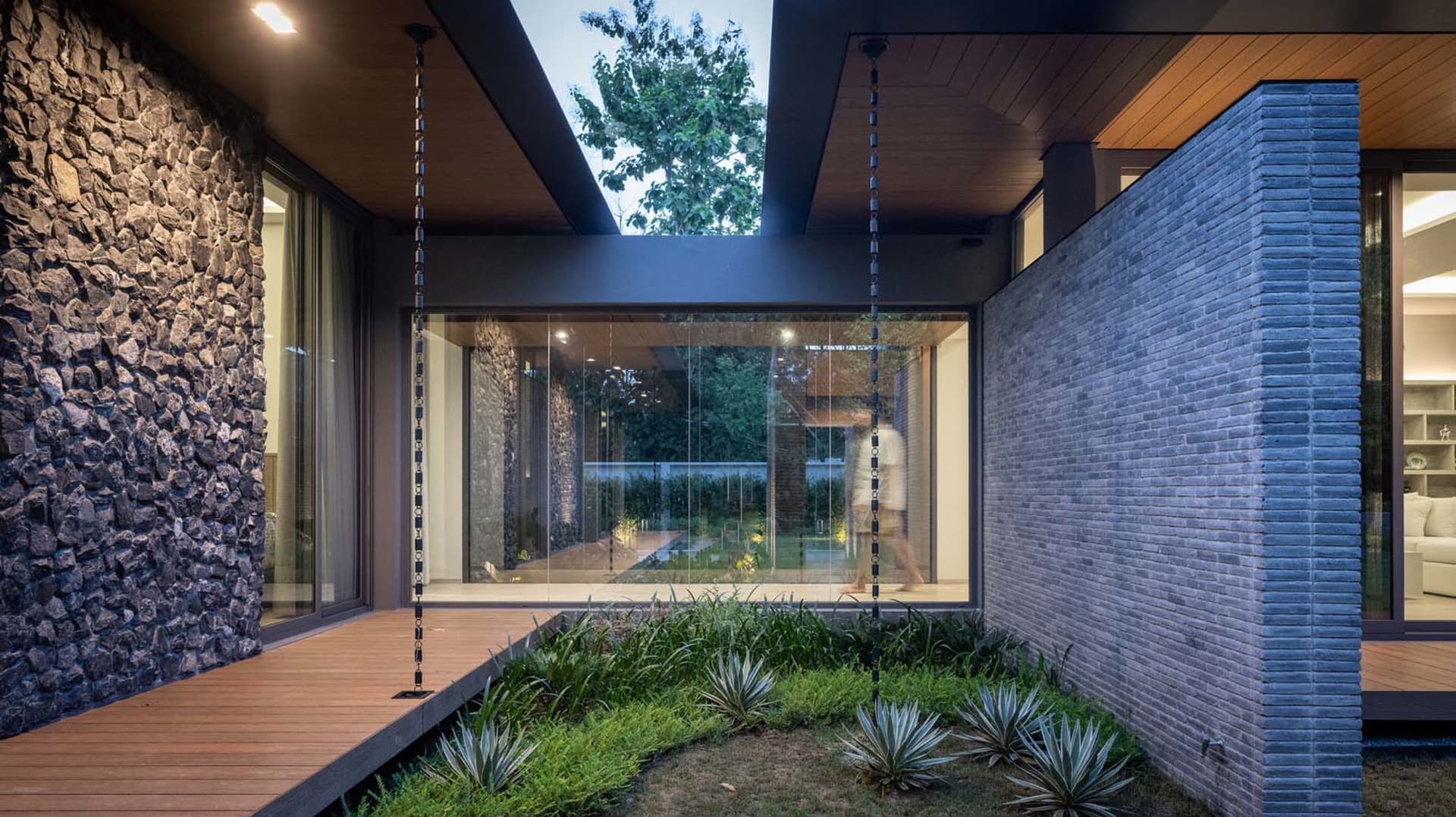 A modern house exterior featuring a wooden deck, stone wall, and greenery.