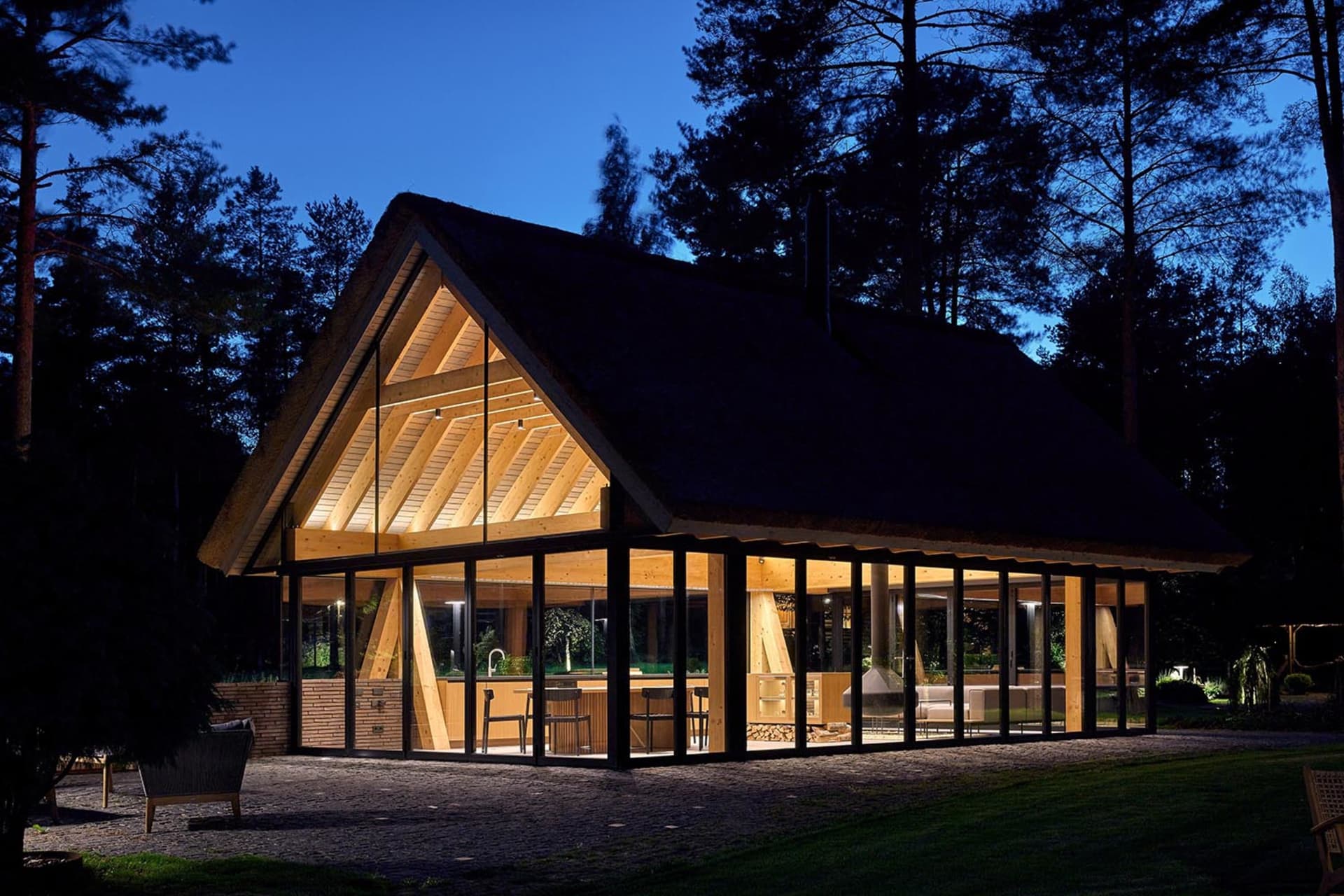 A modern residential building illuminated at night, featuring large glass windows and wooden structural elements.