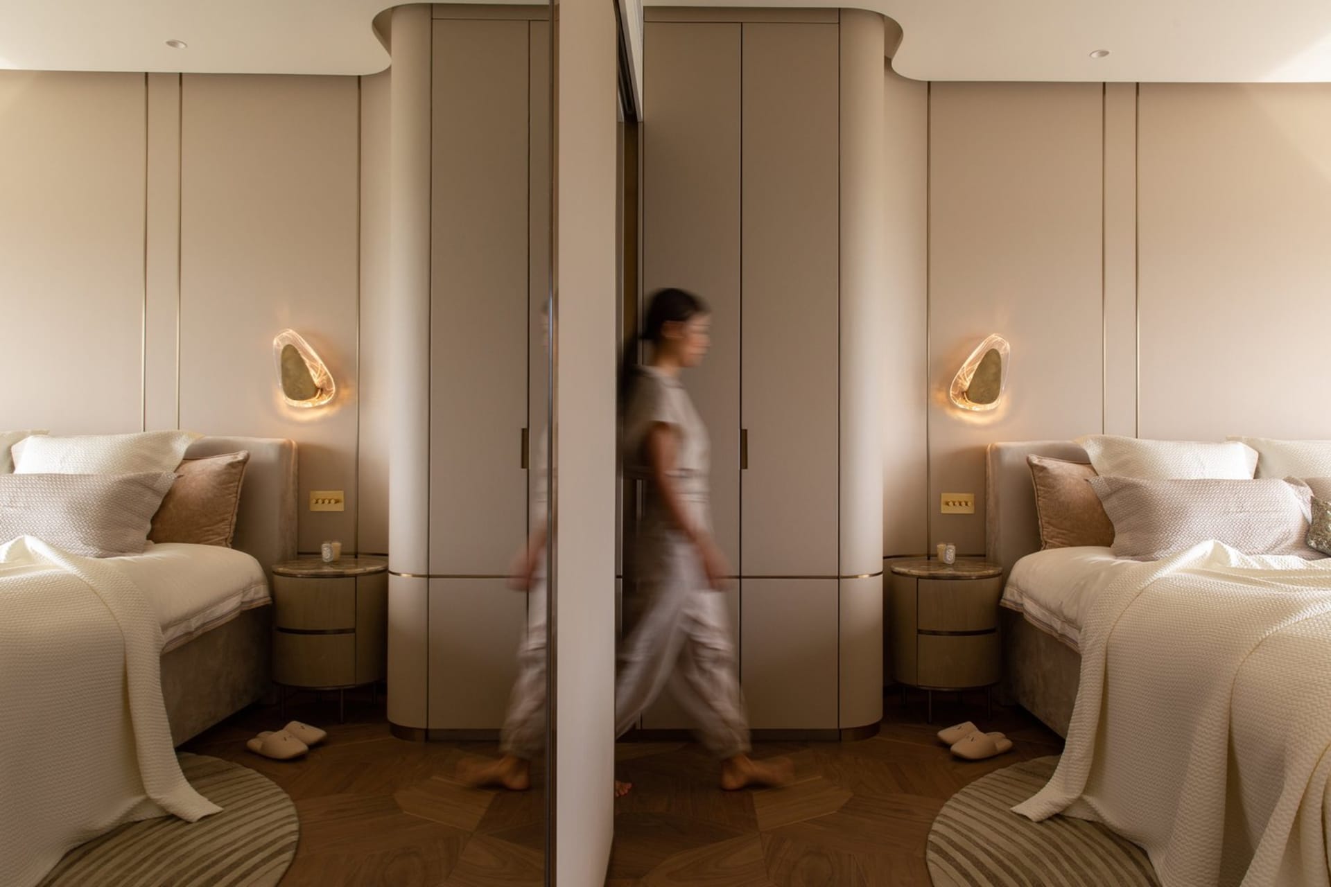 A modern bedroom with neutral-toned walls, flooring, and furnishings, featuring two beds, wall sconces, and a large closet.