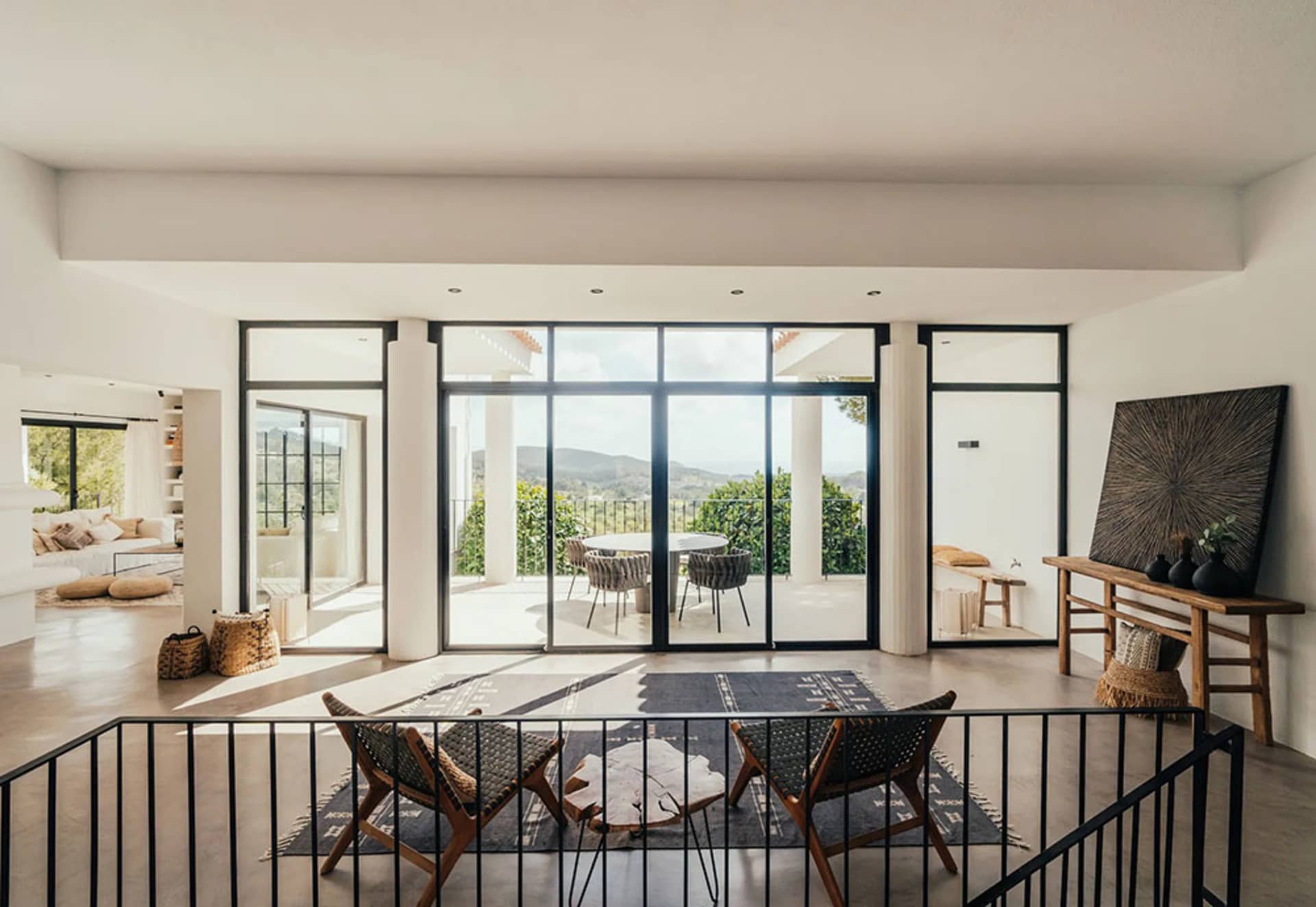 Modern minimalist living room with large glass windows and concrete floor, featuring natural-fiber seating and an outdoor vie