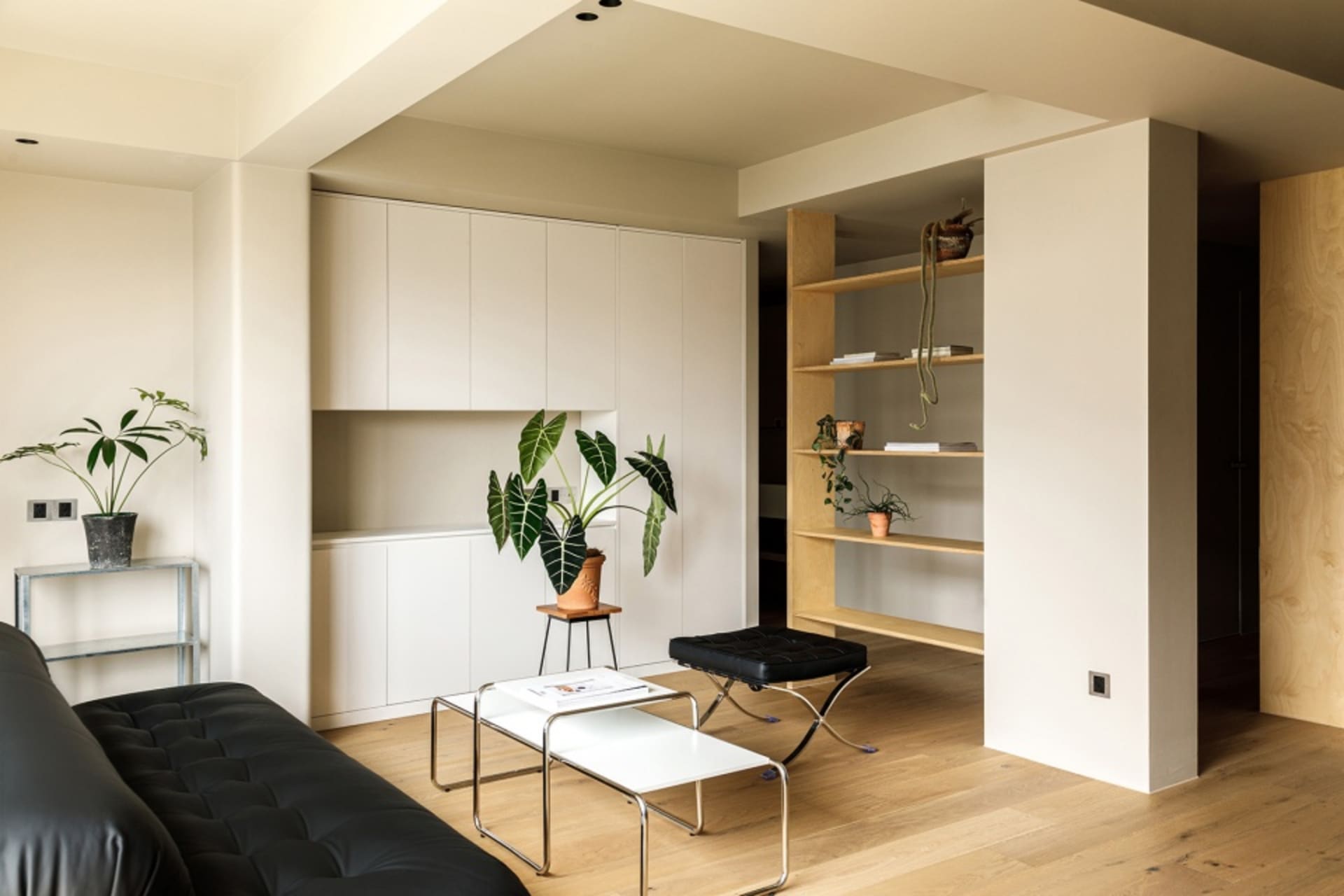 A modern minimalist living room with a black couch, white coffee tables, and wooden flooring.