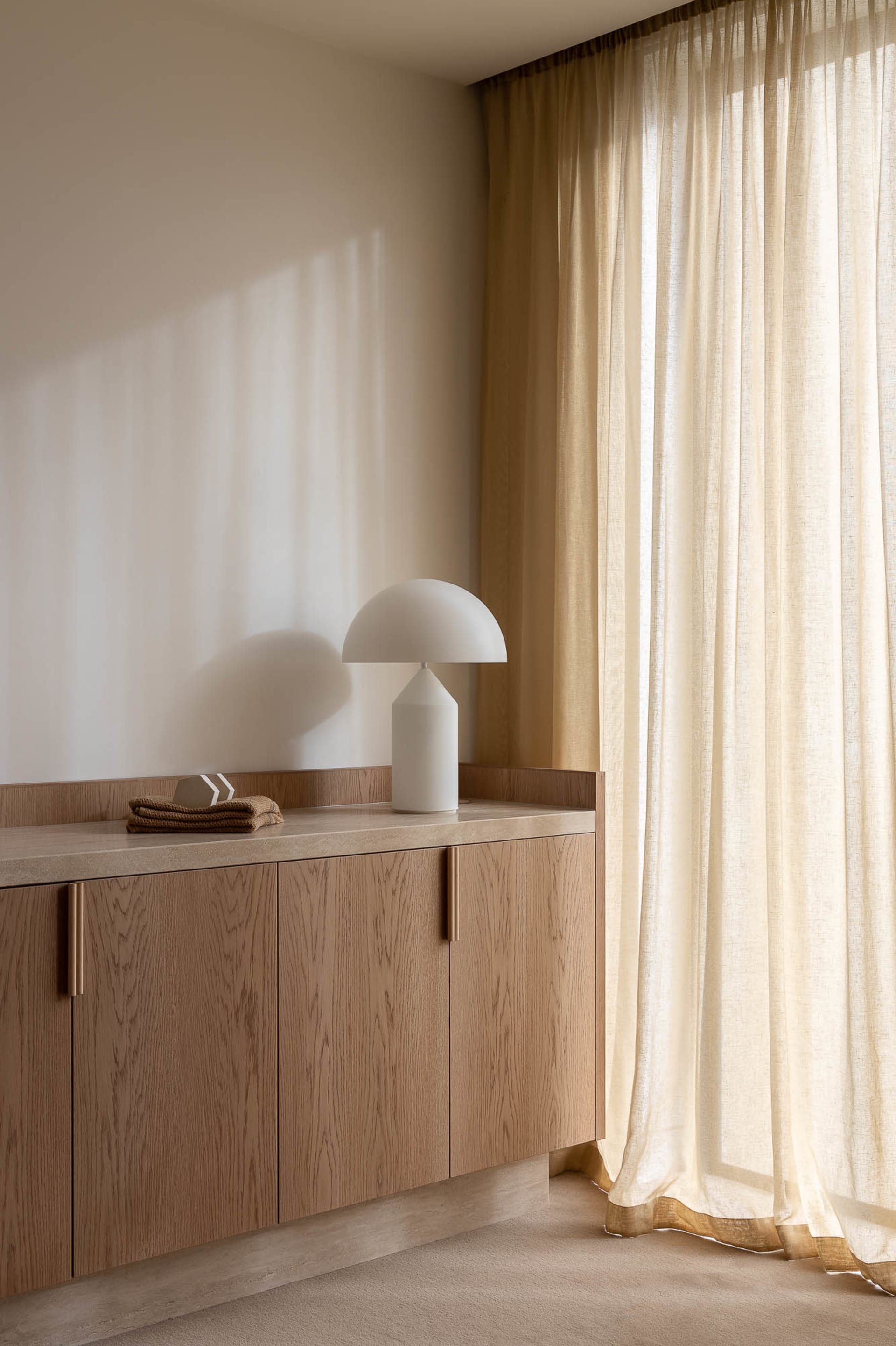 A modern minimalist interior design featuring a wooden cabinet with a white table lamp and a clear glass vase.