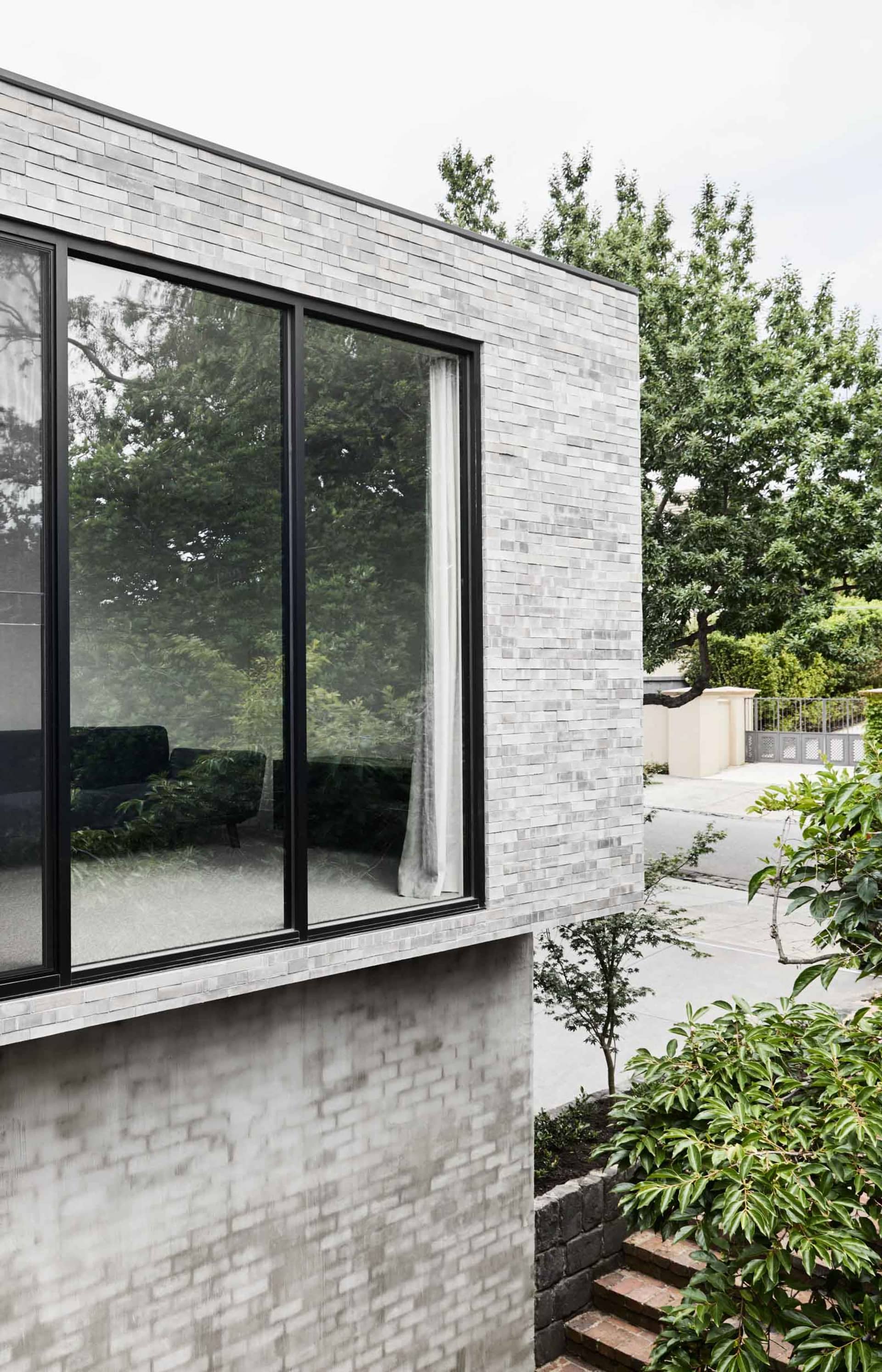 Modern gray brick exterior with large windows reflecting greenery and trees.