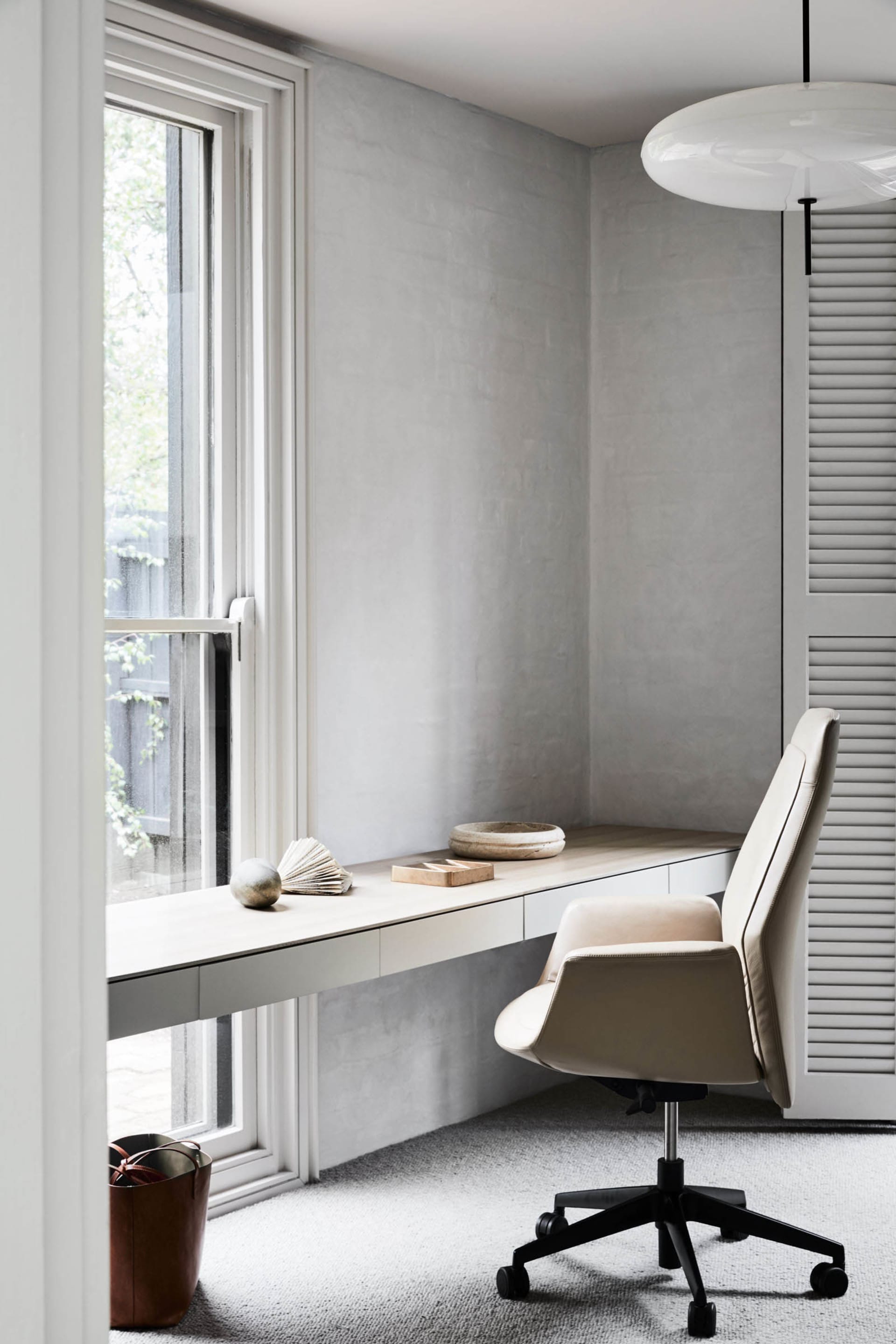 A modern office with a light wood desk, minimalist chair, and minimalist decor by a window.