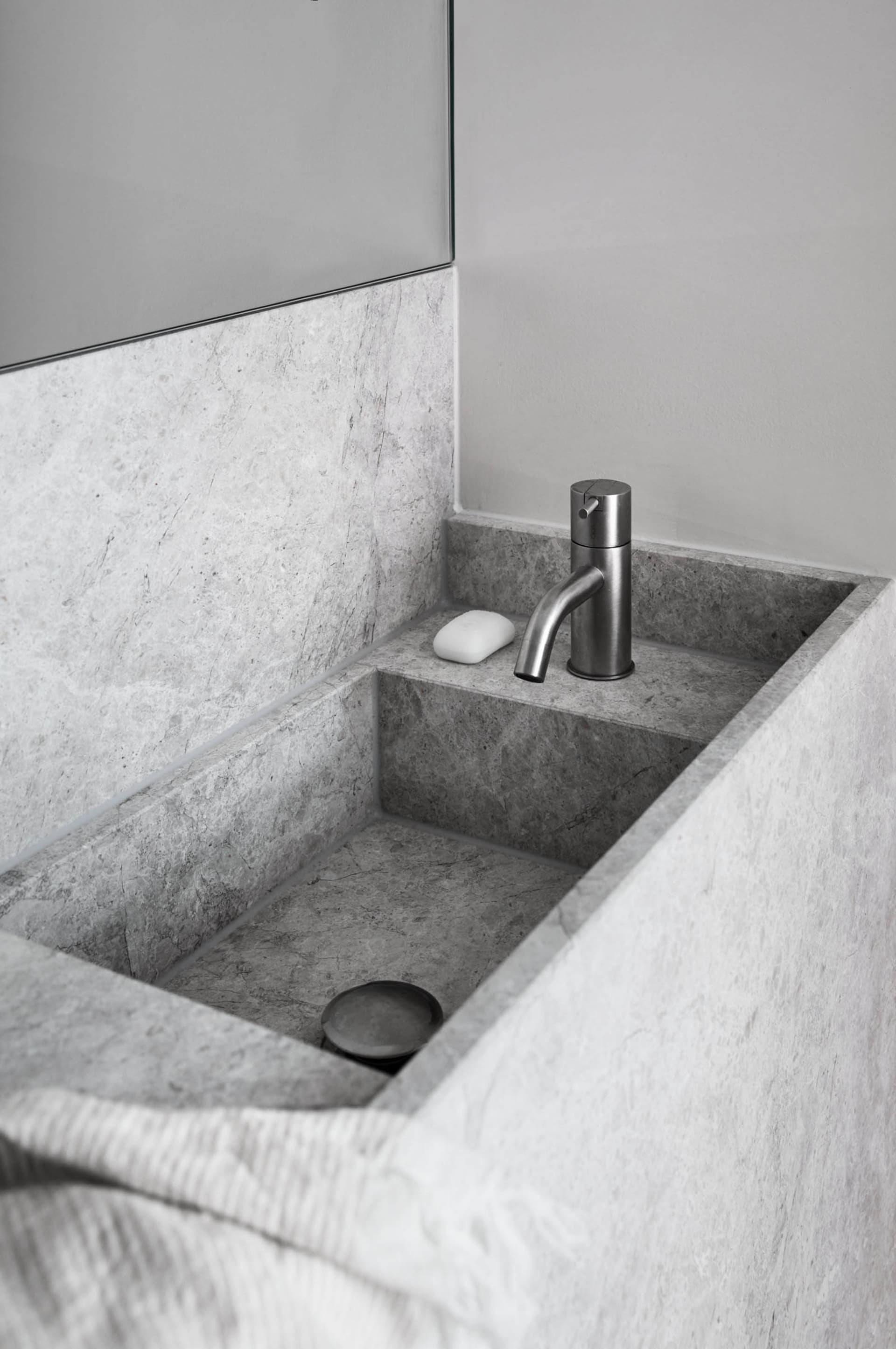 A minimalist bathroom with a concrete sink and a stainless steel faucet.