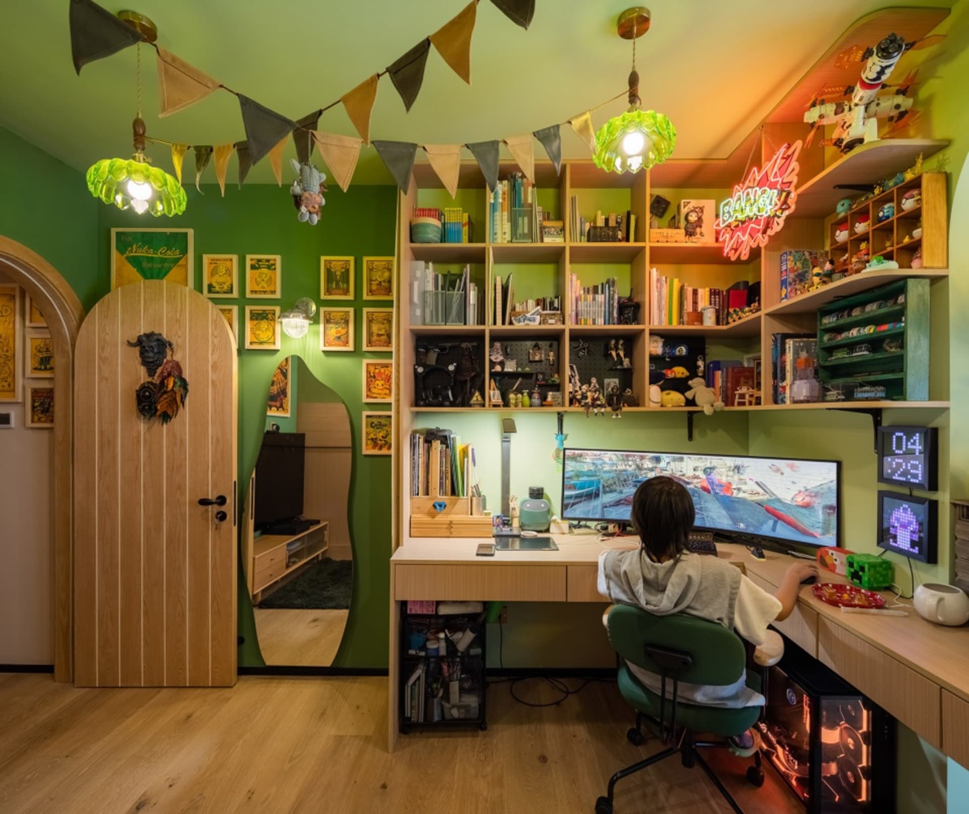 A modern playroom with green wooden shelves, a child sitting at a desk playing a video game, and various toys and books on th