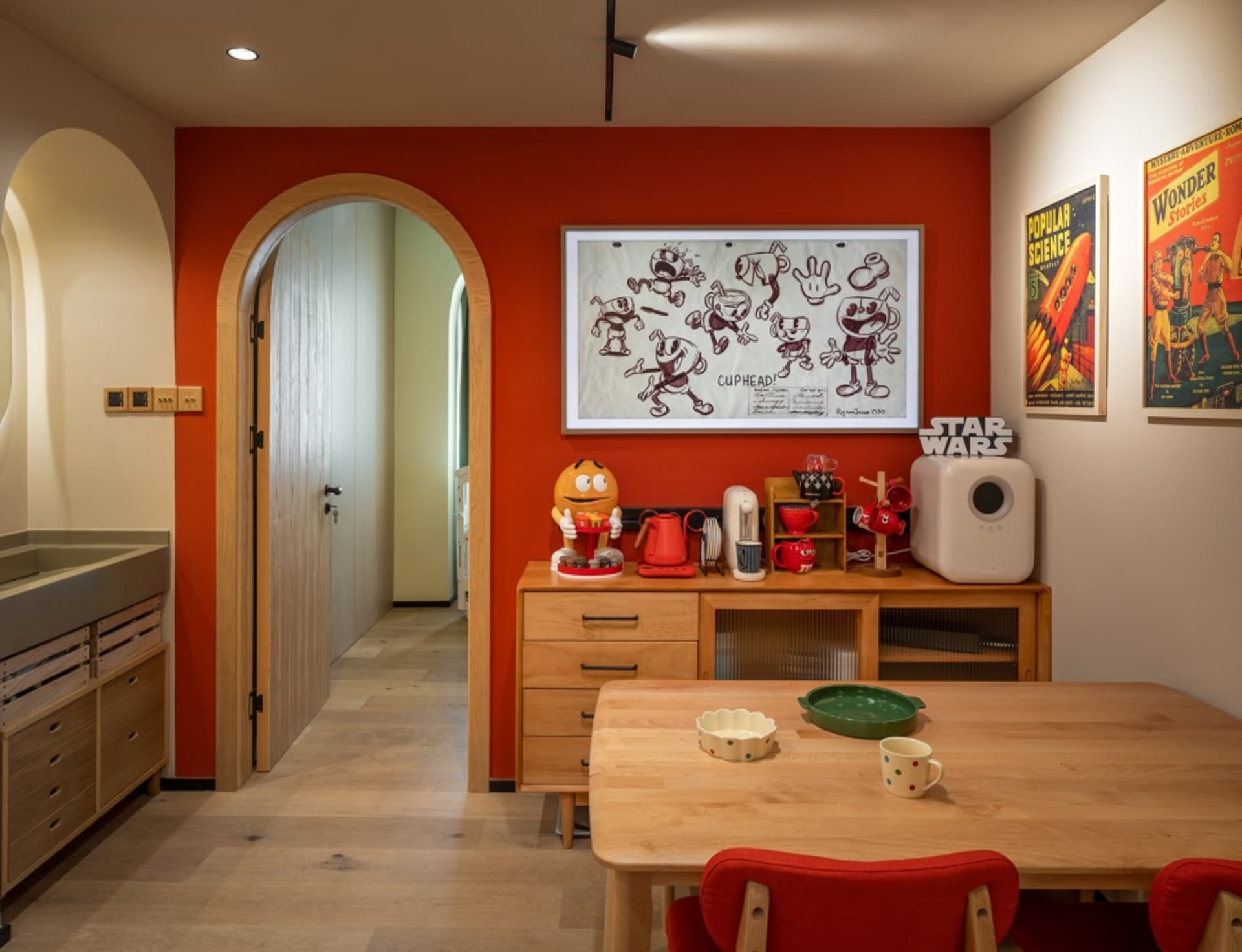 A modern kitchen interior with a red accent wall, wooden table, and various decorative items.