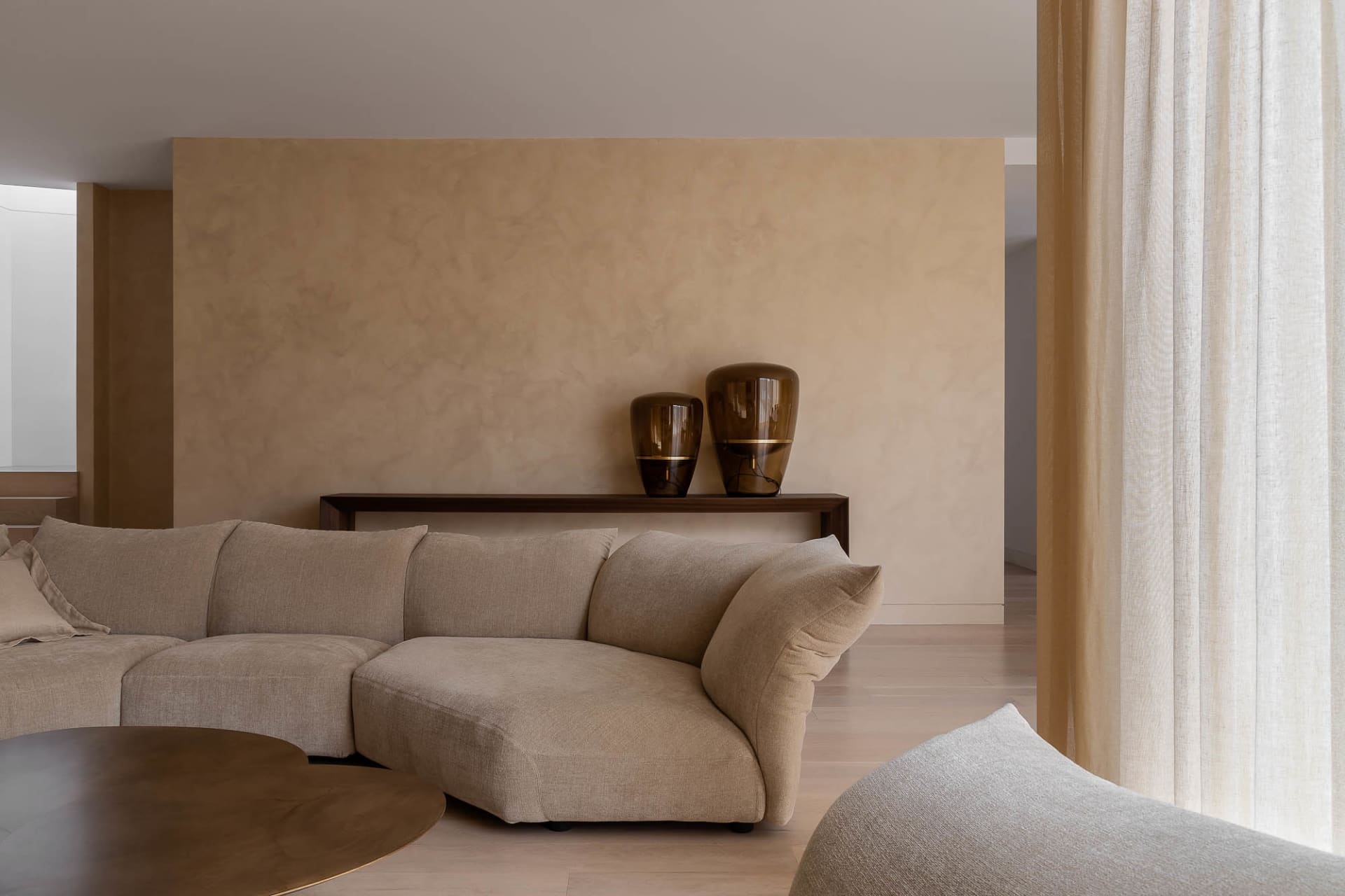A modern living room with a neutral-toned sofa, minimalist decor, and large windows.