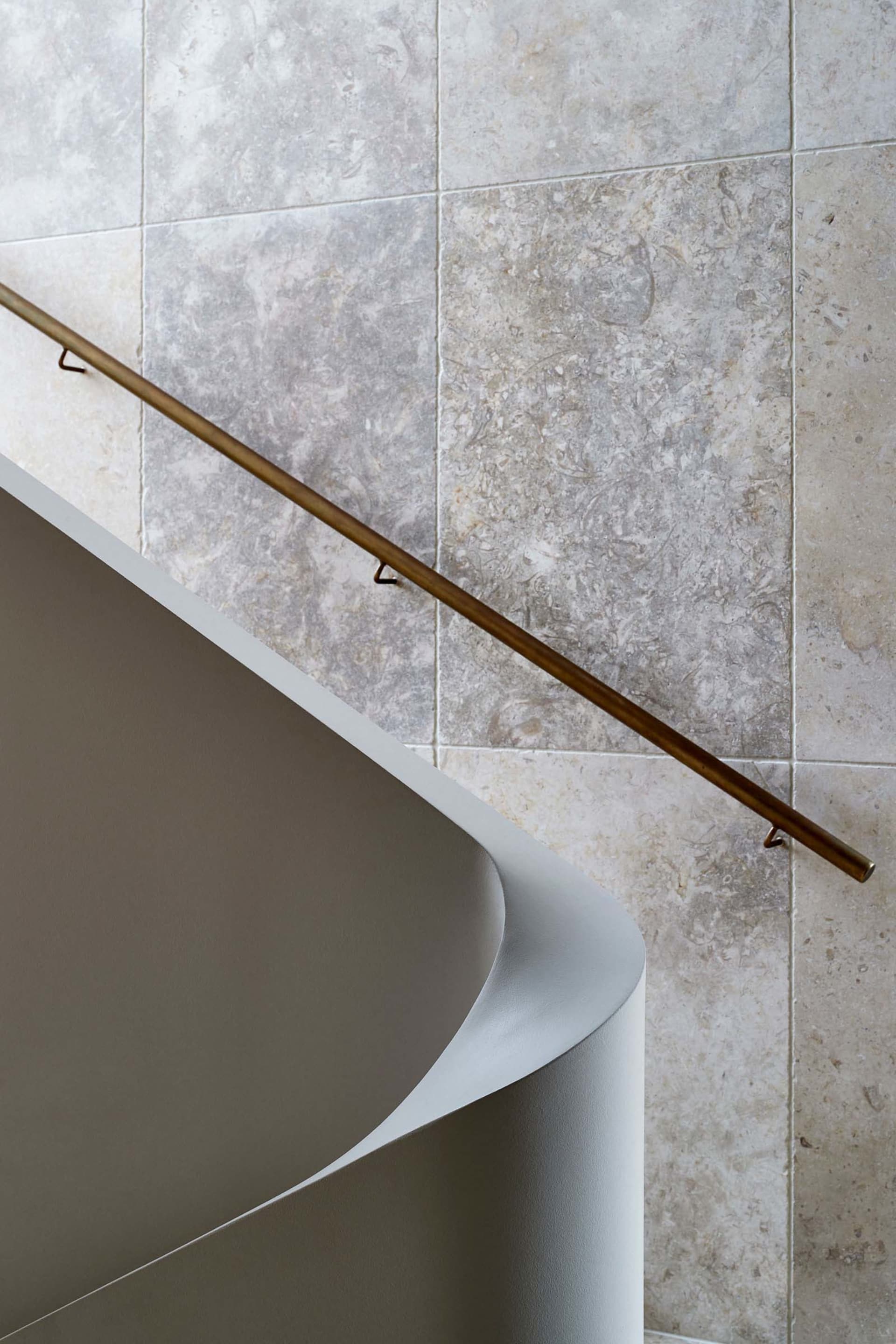 A modern staircase featuring a bronze metal railing against a textured wall.