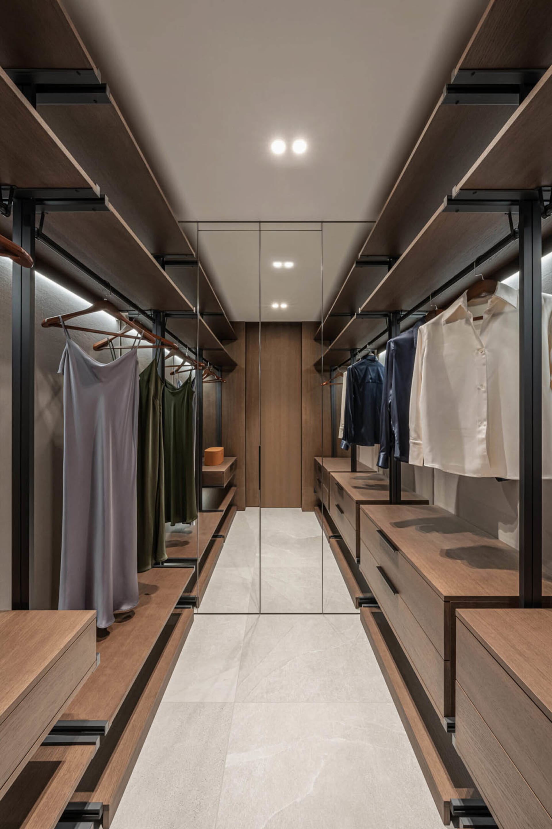 A modern closet with wood shelves, hanging clothes, and a mirrored door.