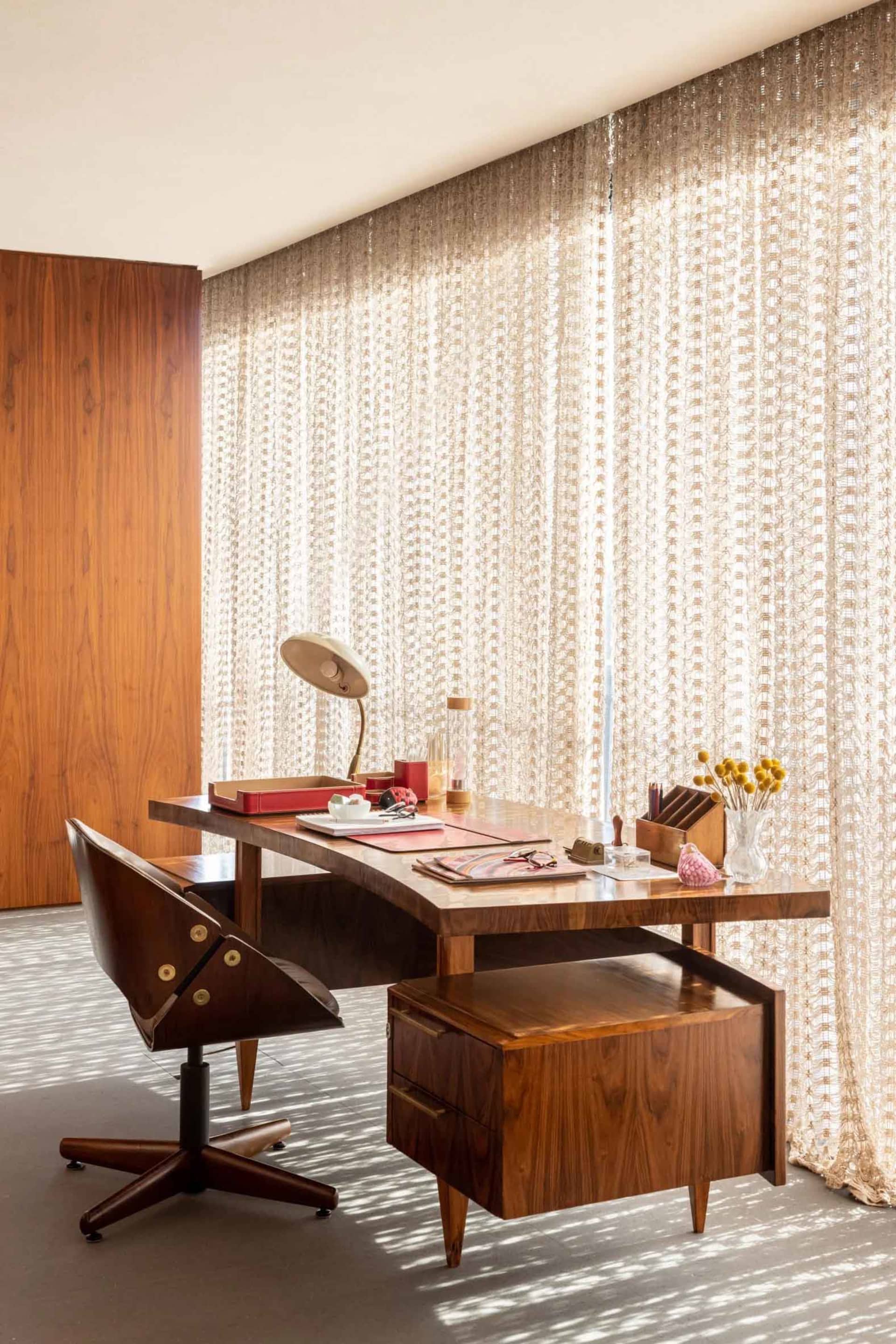 A modern industrial home office with a wooden desk and swivel chair, featuring a red desk organizer and a lamp.