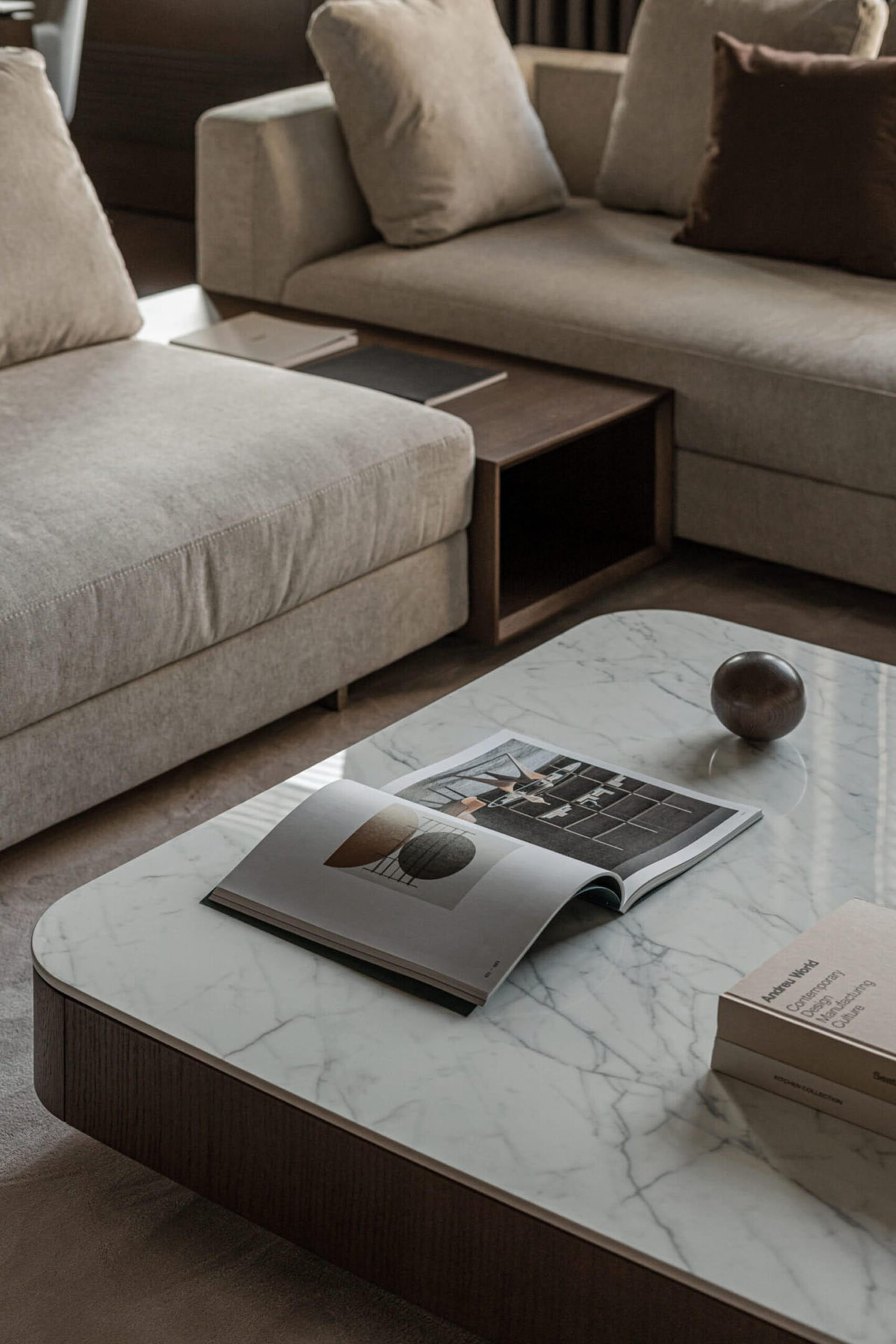 Modern living room with beige sofas, marble coffee table, and books.