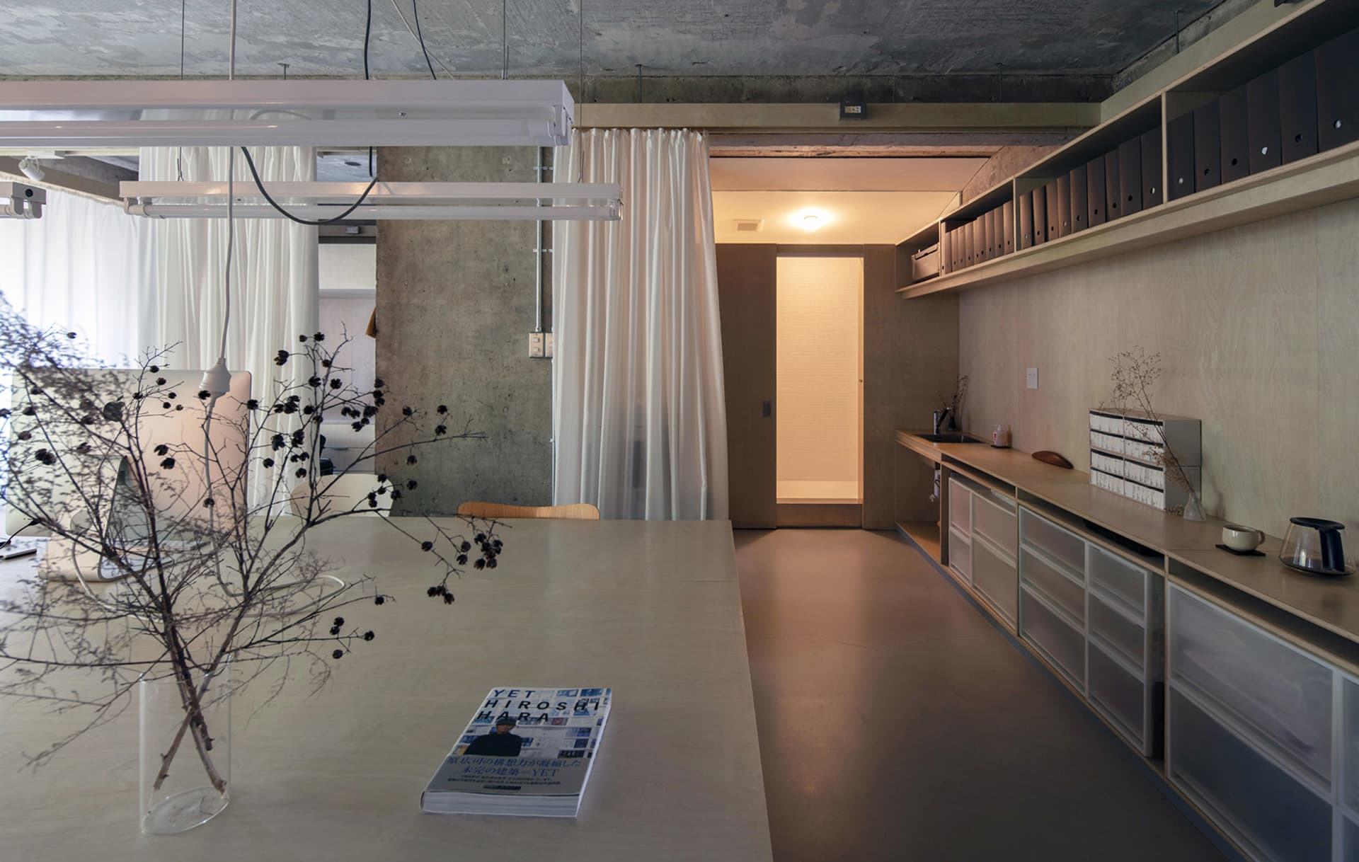 Minimalist office interior with concrete walls, wooden furniture, and white curtains.