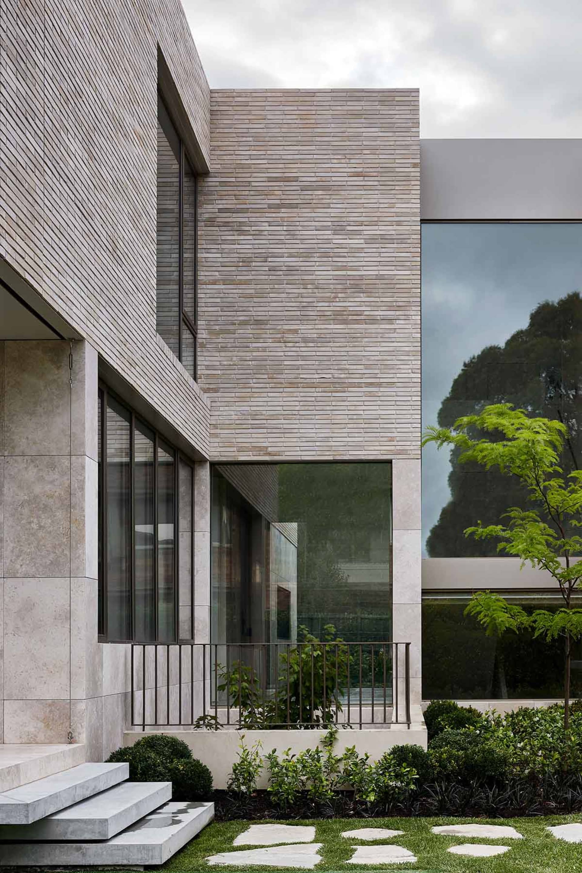 Modern residential exterior featuring brick and stone materials and large glass windows.