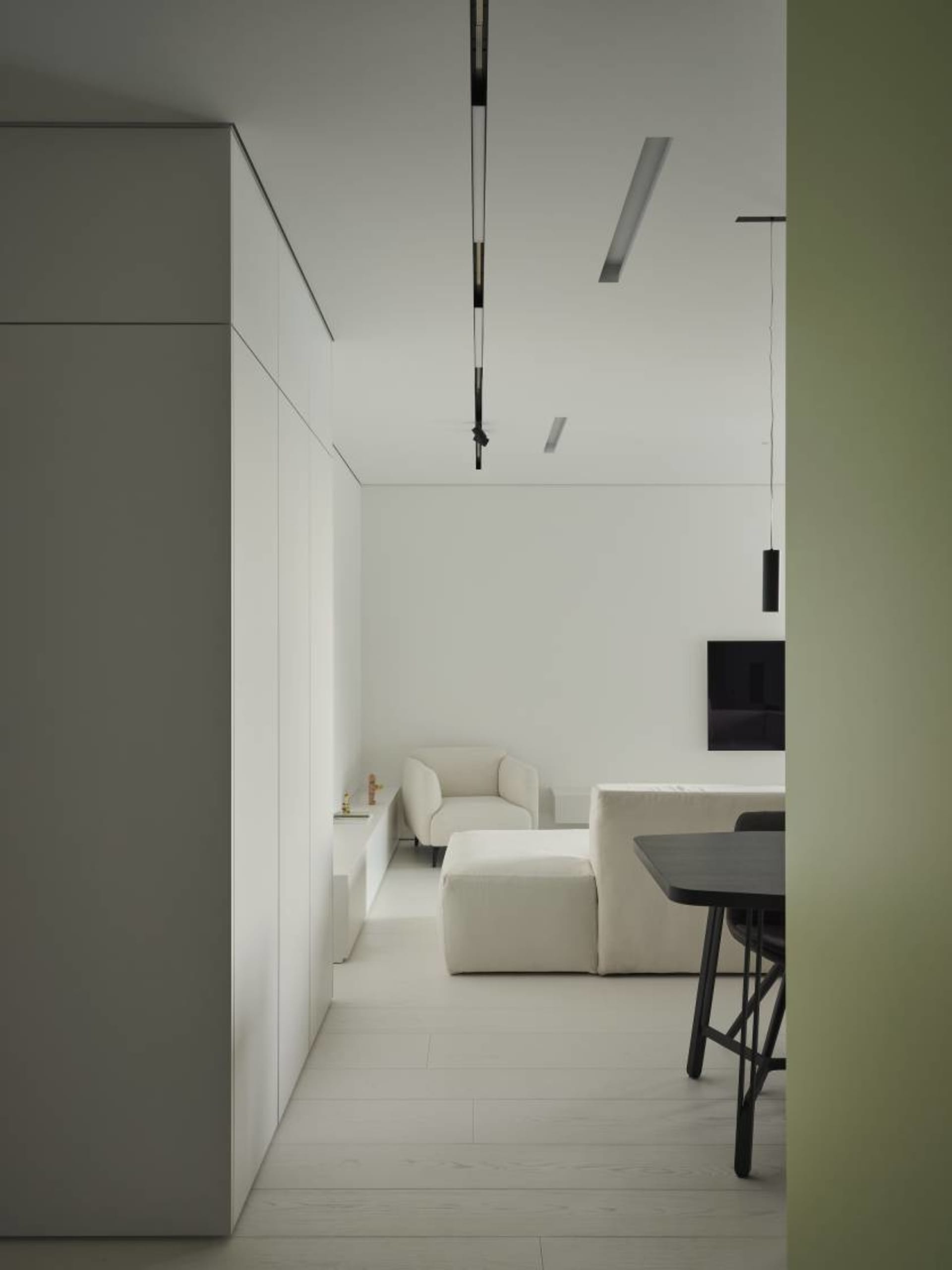 A minimalist living room with white furniture, white walls, and light-colored wood flooring.