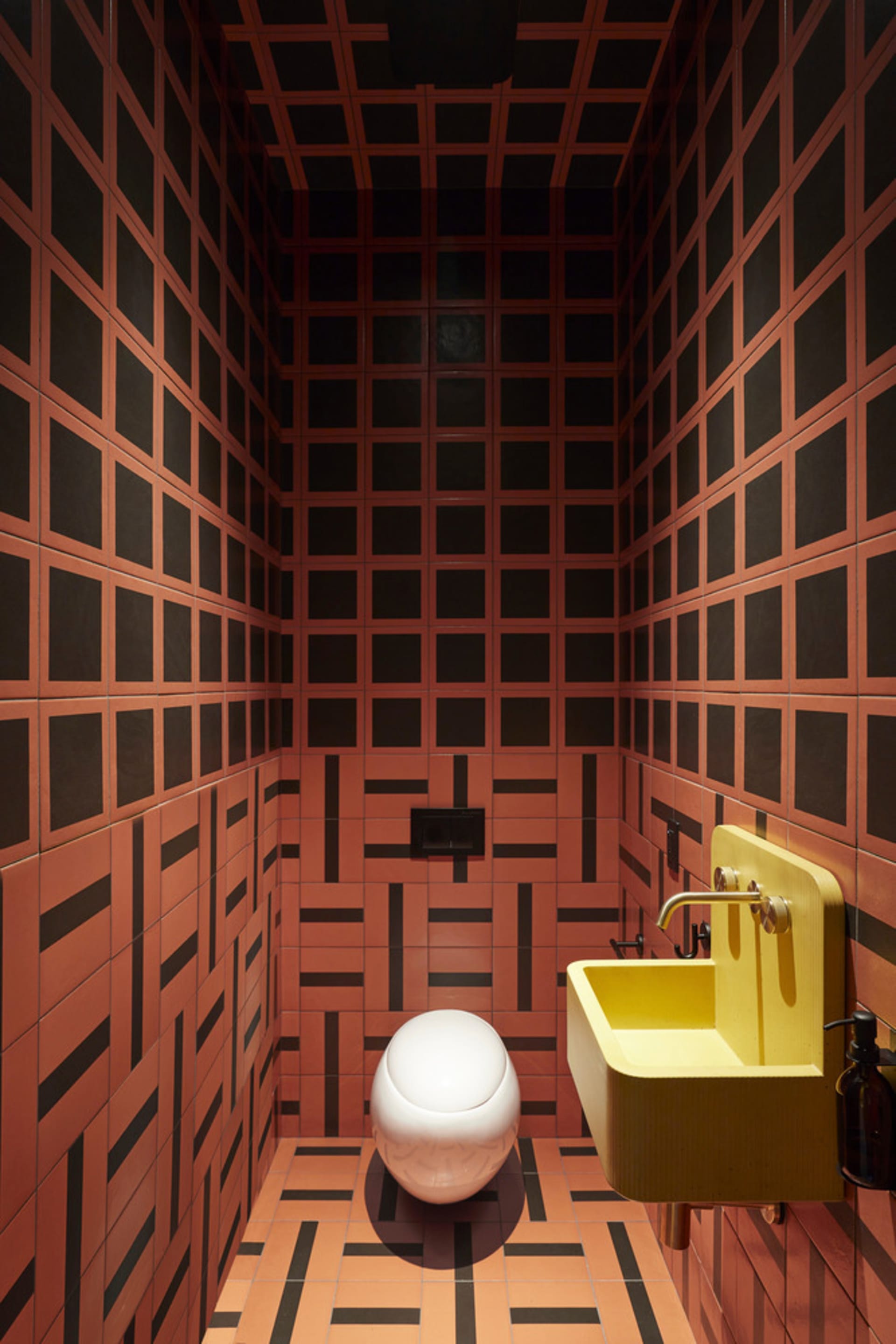 A modern industrial bathroom with a striking patterned tile design, featuring a contemporary toilet and a vibrant yellow sink