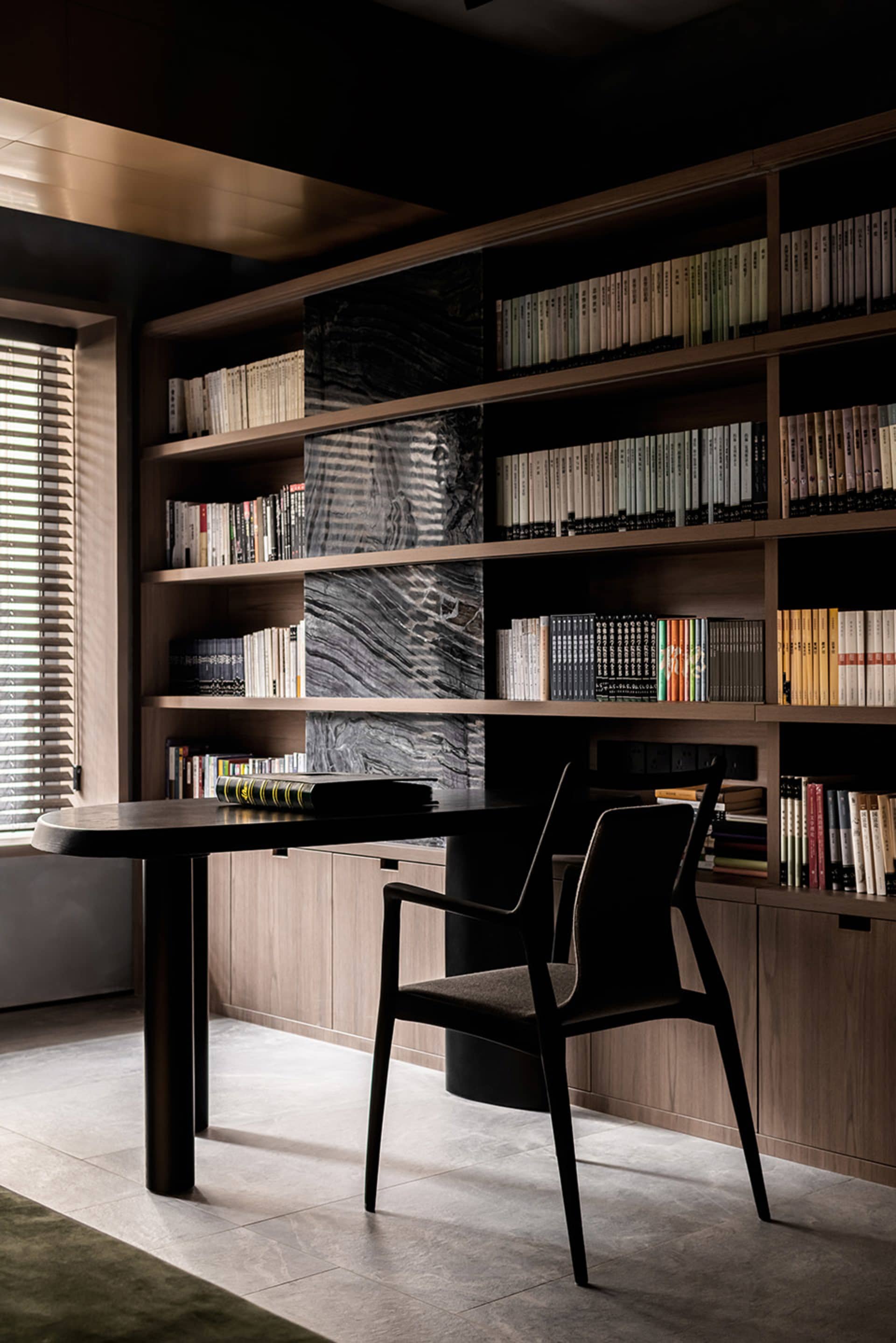 A modern study room featuring a sleek, black wooden desk and a large wooden bookshelf filled with books arranged neatly. The