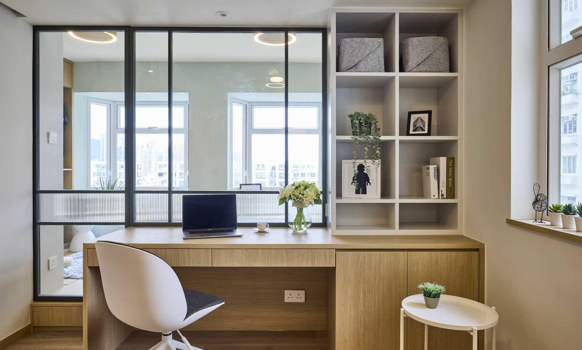 A modern home office with a wooden desk, white chair, and bookshelf.