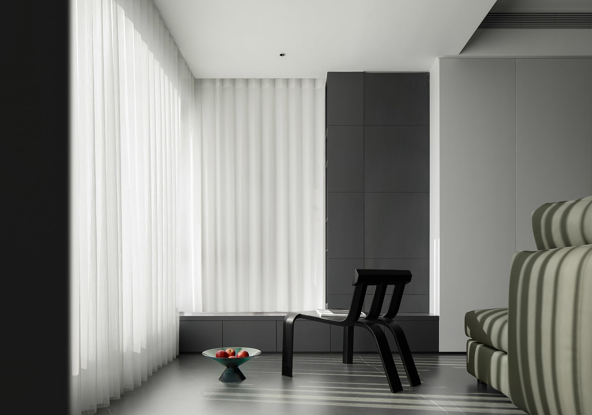 A modern minimalist living room with curtains, a black sculptural chair, and a white couch with vertical stripes.