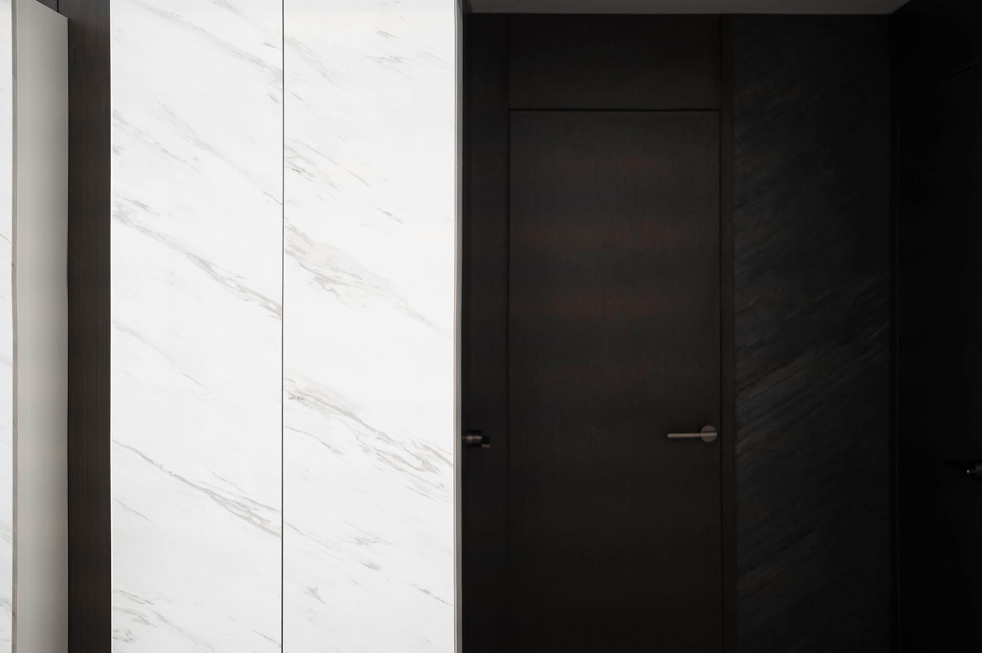 A modern, minimalist doorway featuring a white marble wall and a dark wooden door.
