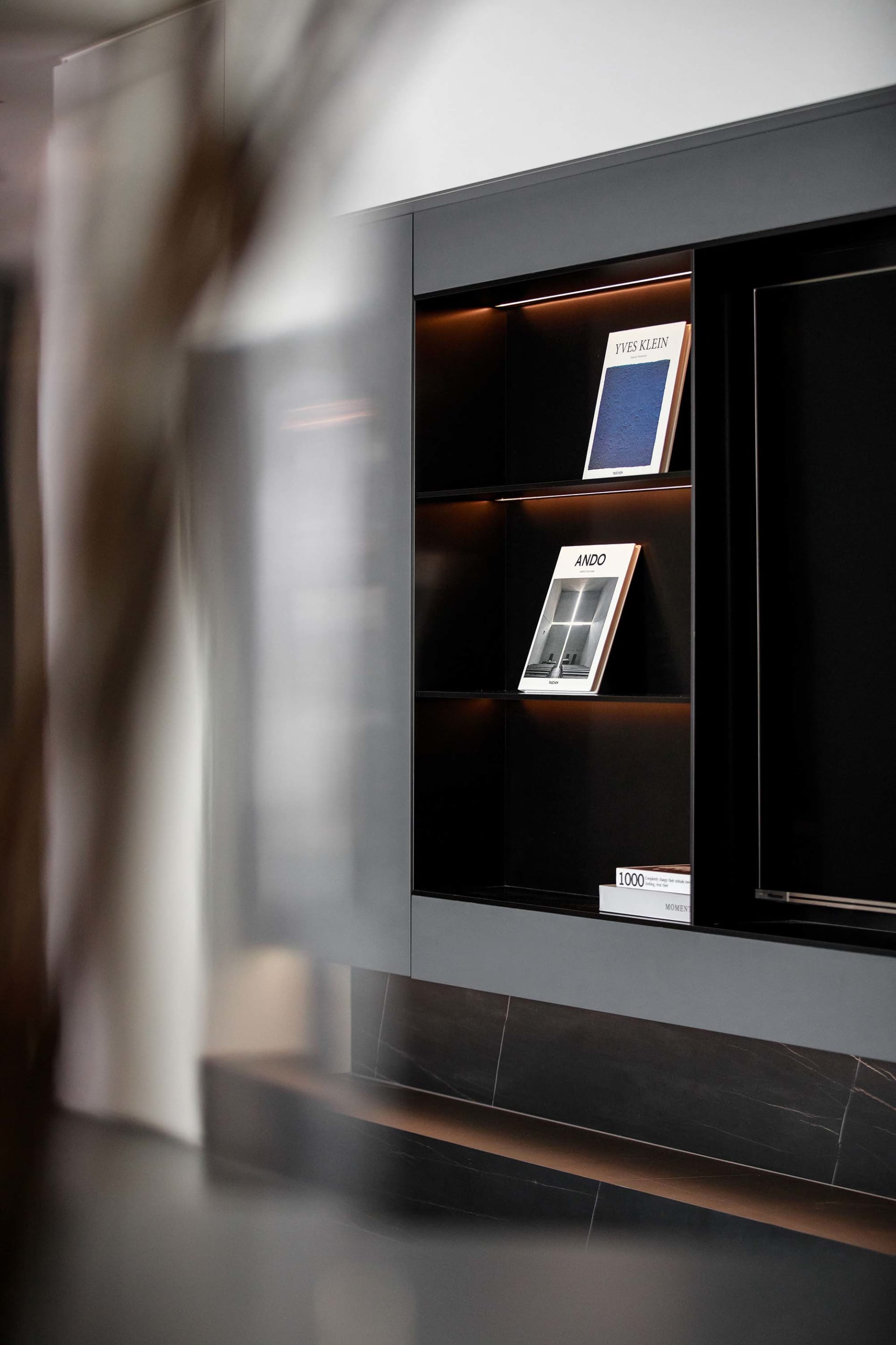 A modern bookshelf with dark wood and glass shelves displaying books.