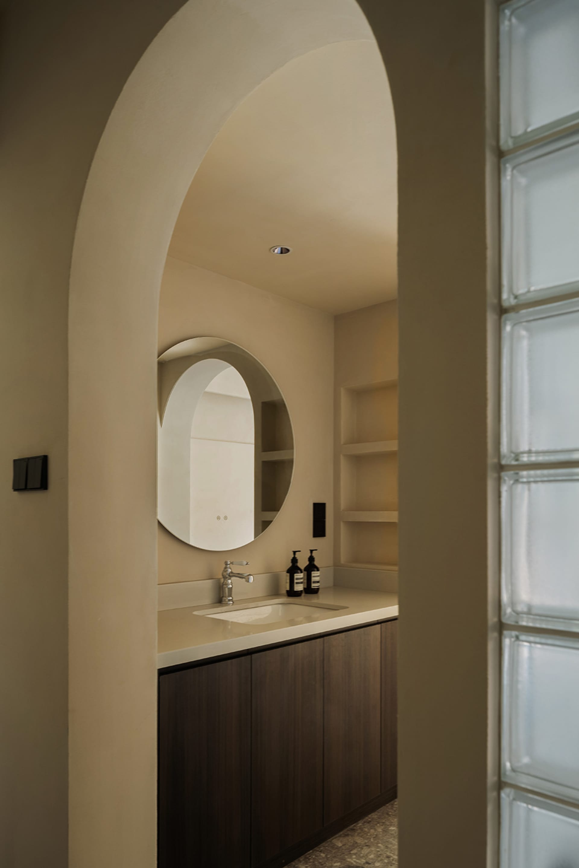 A minimalist bathroom with a concrete counter, sink, and round mirror.