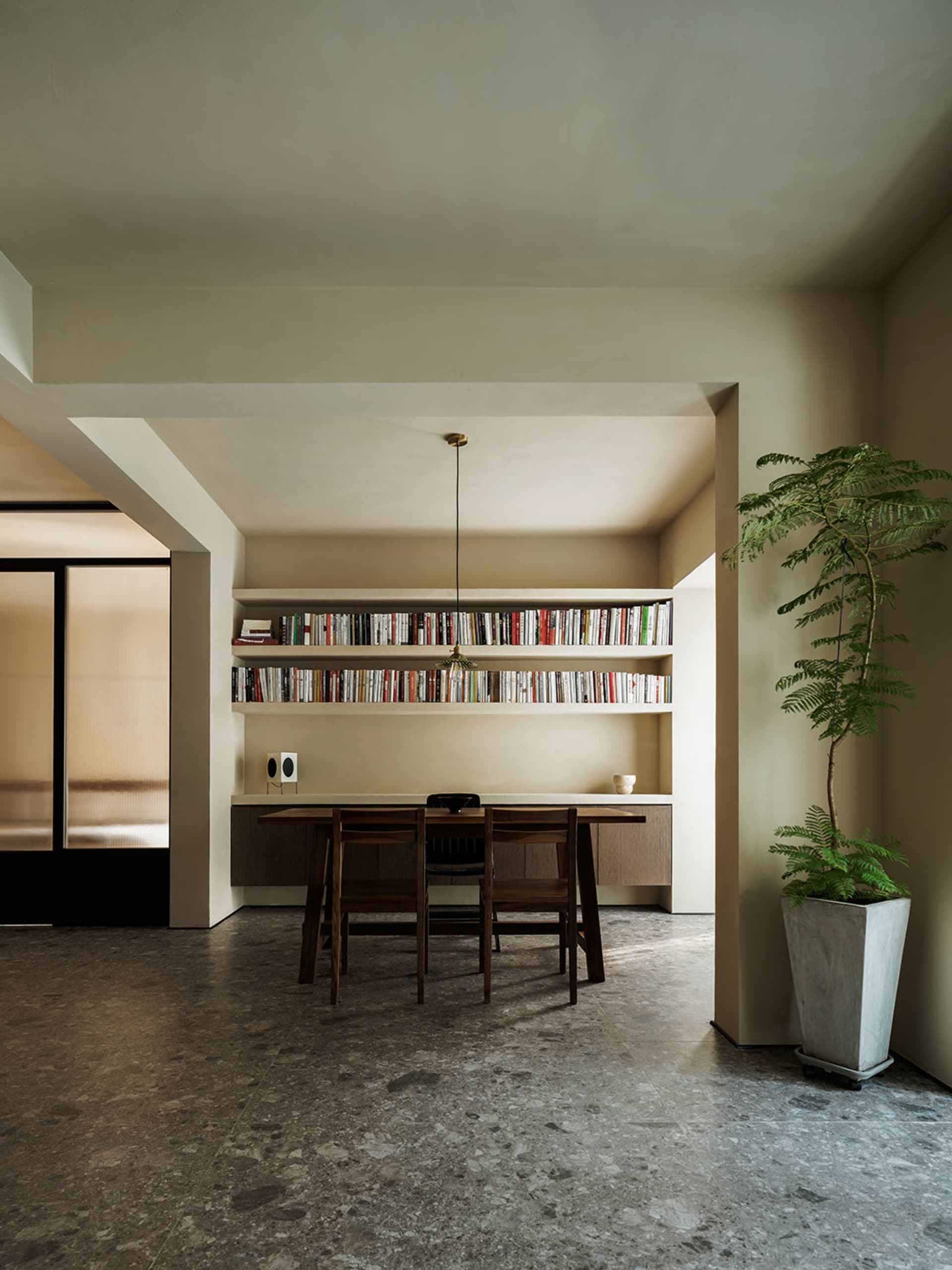 A minimalist dining area featuring a concrete table and chairs with built-in bookshelves.