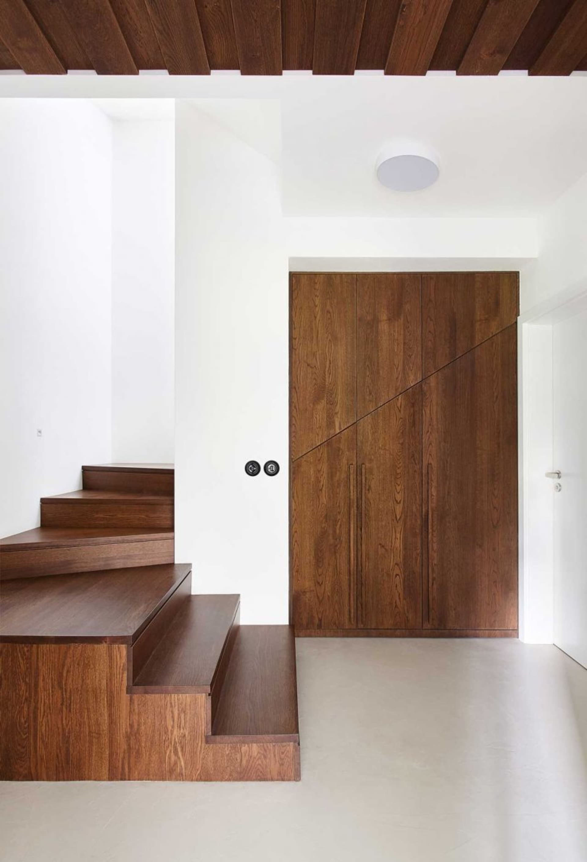 A modern staircase entryway with wooden paneling, featuring white walls and a ceiling.
