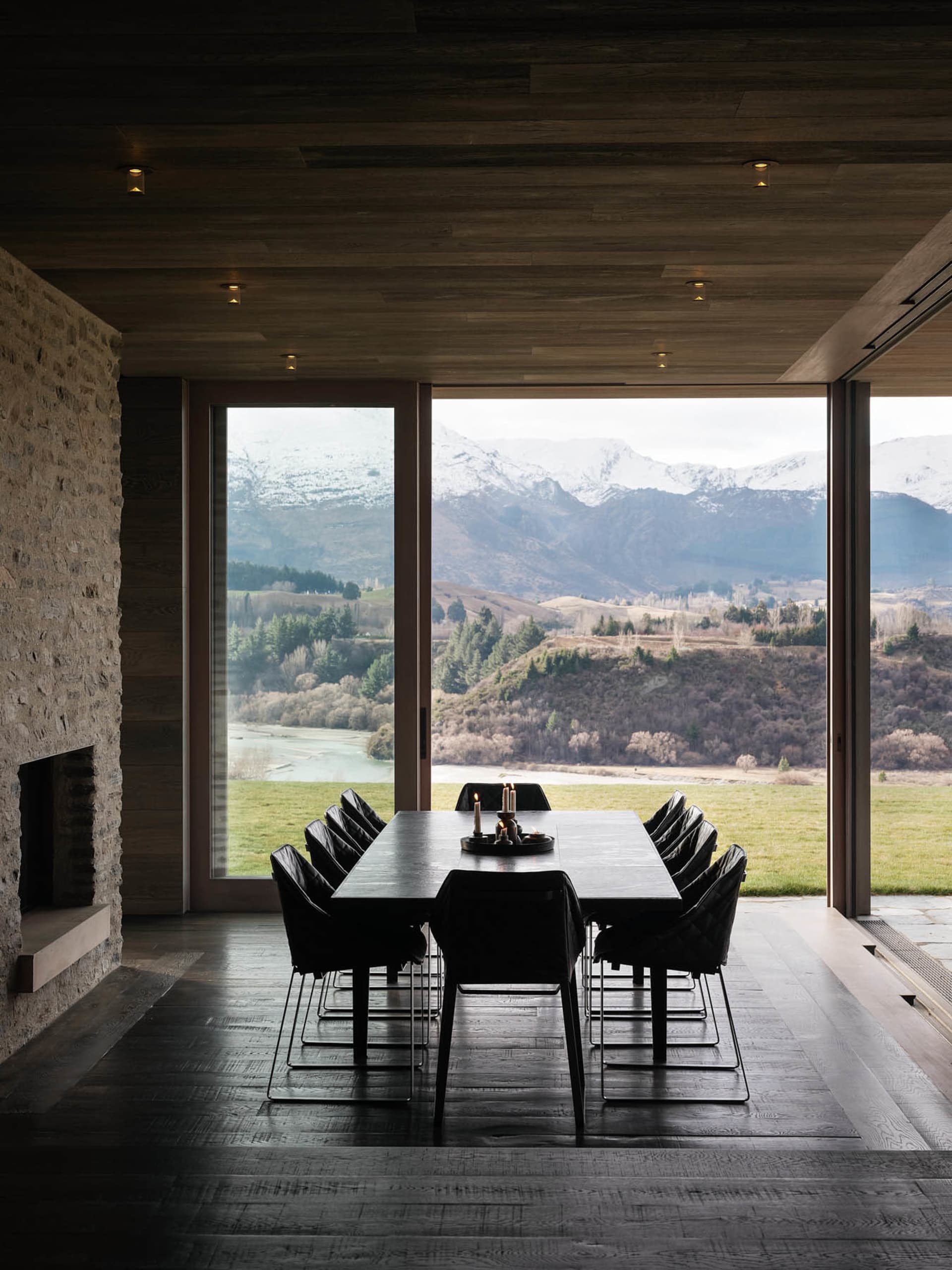 An elegant dining room with large windows showcasing a picturesque mountain landscape, featuring modern black wooden table an