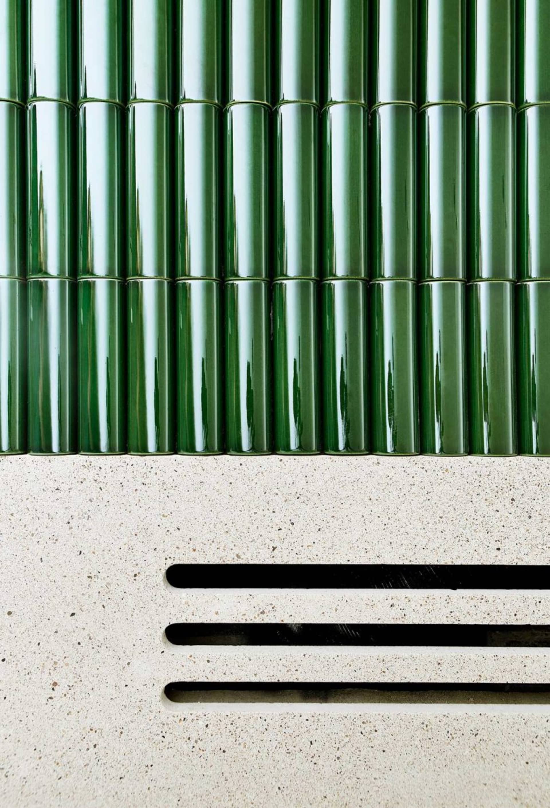 Green tiled wall with a white concrete base featuring horizontal slits.