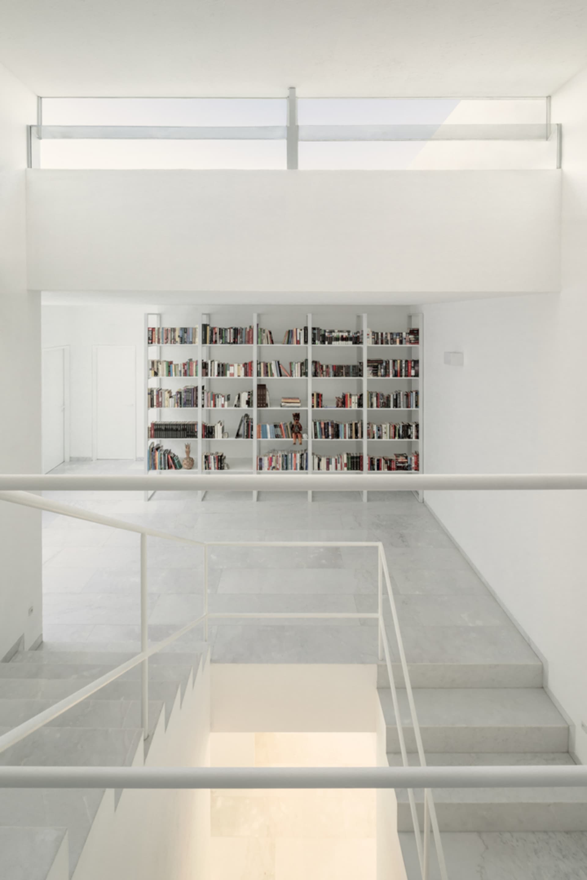 Modern white-shelved library with concrete floor and large glass window.