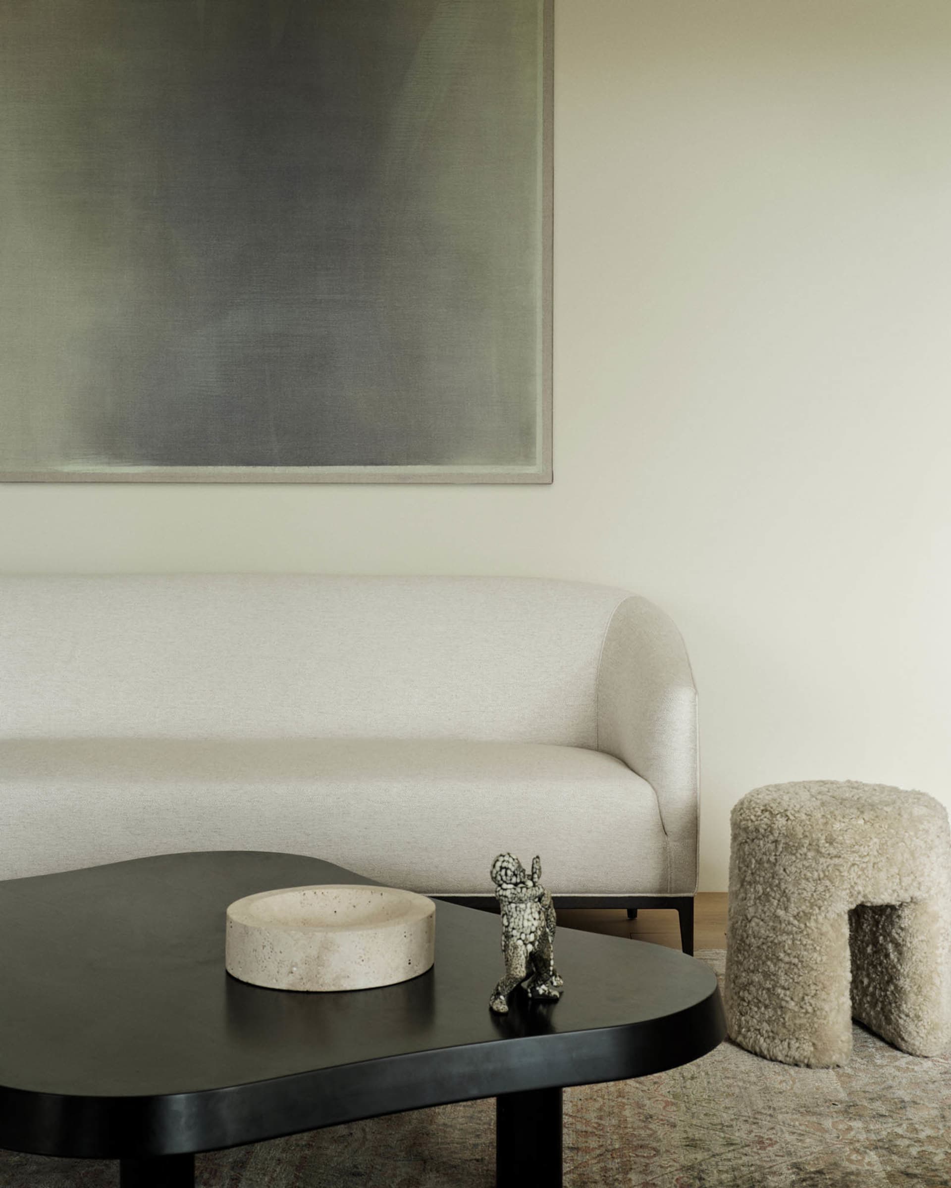A modern living room featuring a beige upholstered sofa, a black coffee table with a concrete bowl and a small sculpture, and