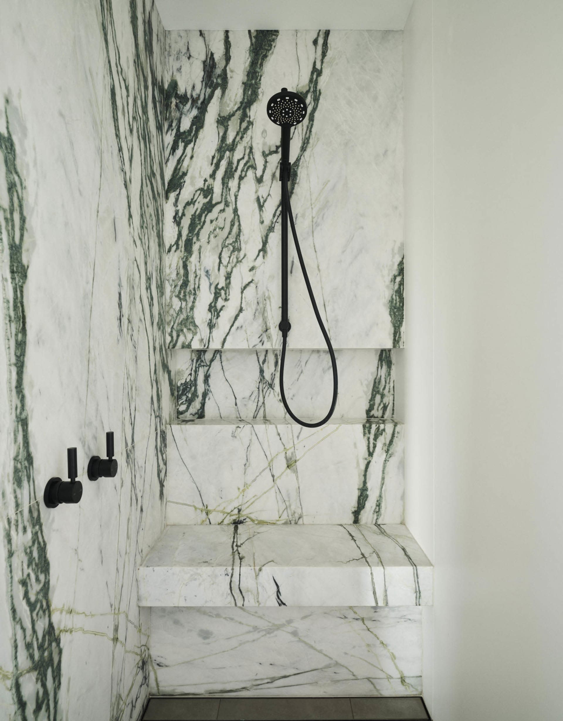 A modern bathroom featuring marble walls and steps with a black showerhead and fixtures.