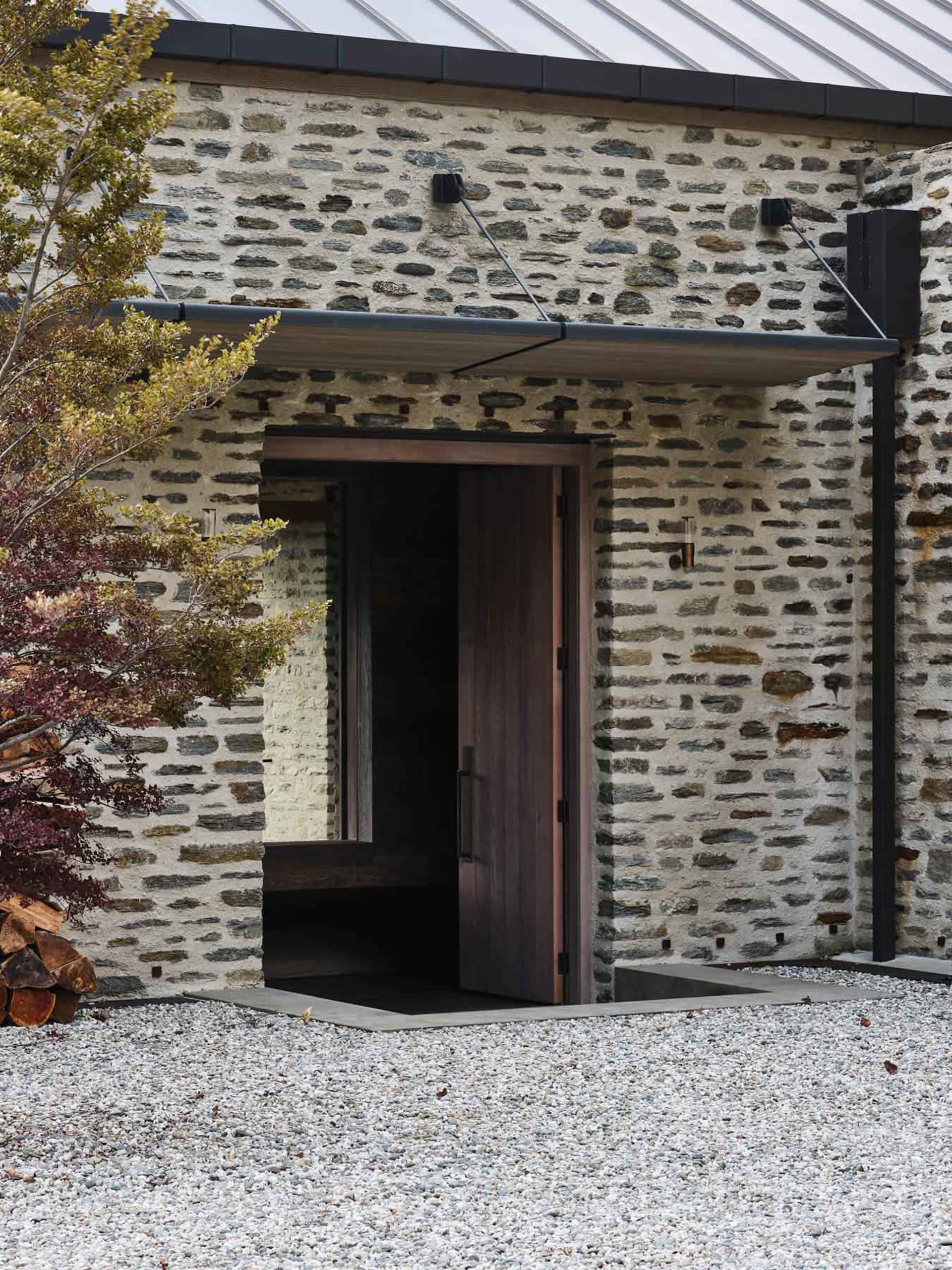 A building entrance made of stone with a wooden door and gravel pathway.